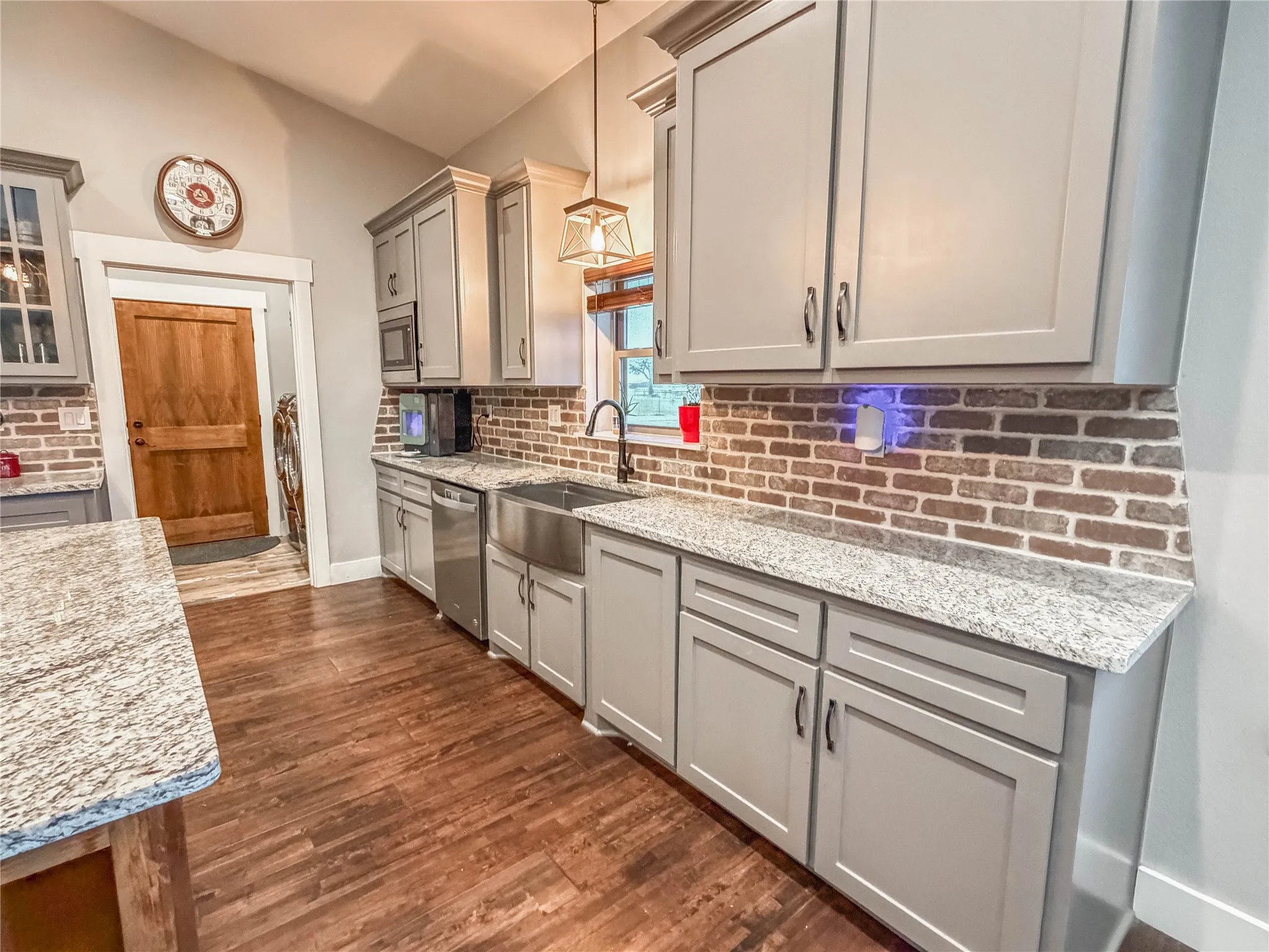 Kitchen with gray cabinets, dark wood-style floors, light stone counters, dishwasher, and hanging light fixtures