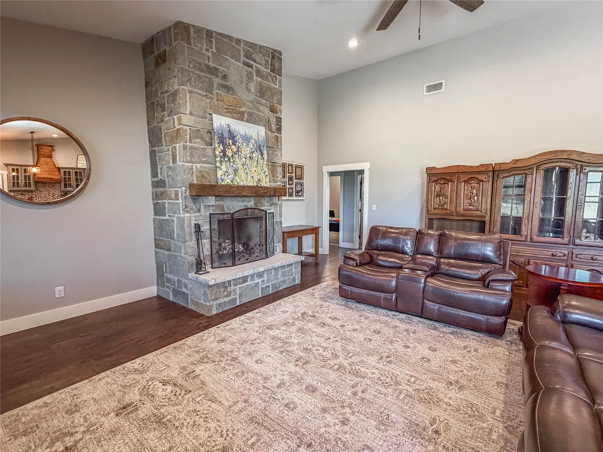 Living area with a stone fireplace, dark wood-style floors, ceiling fan, and a high ceiling
