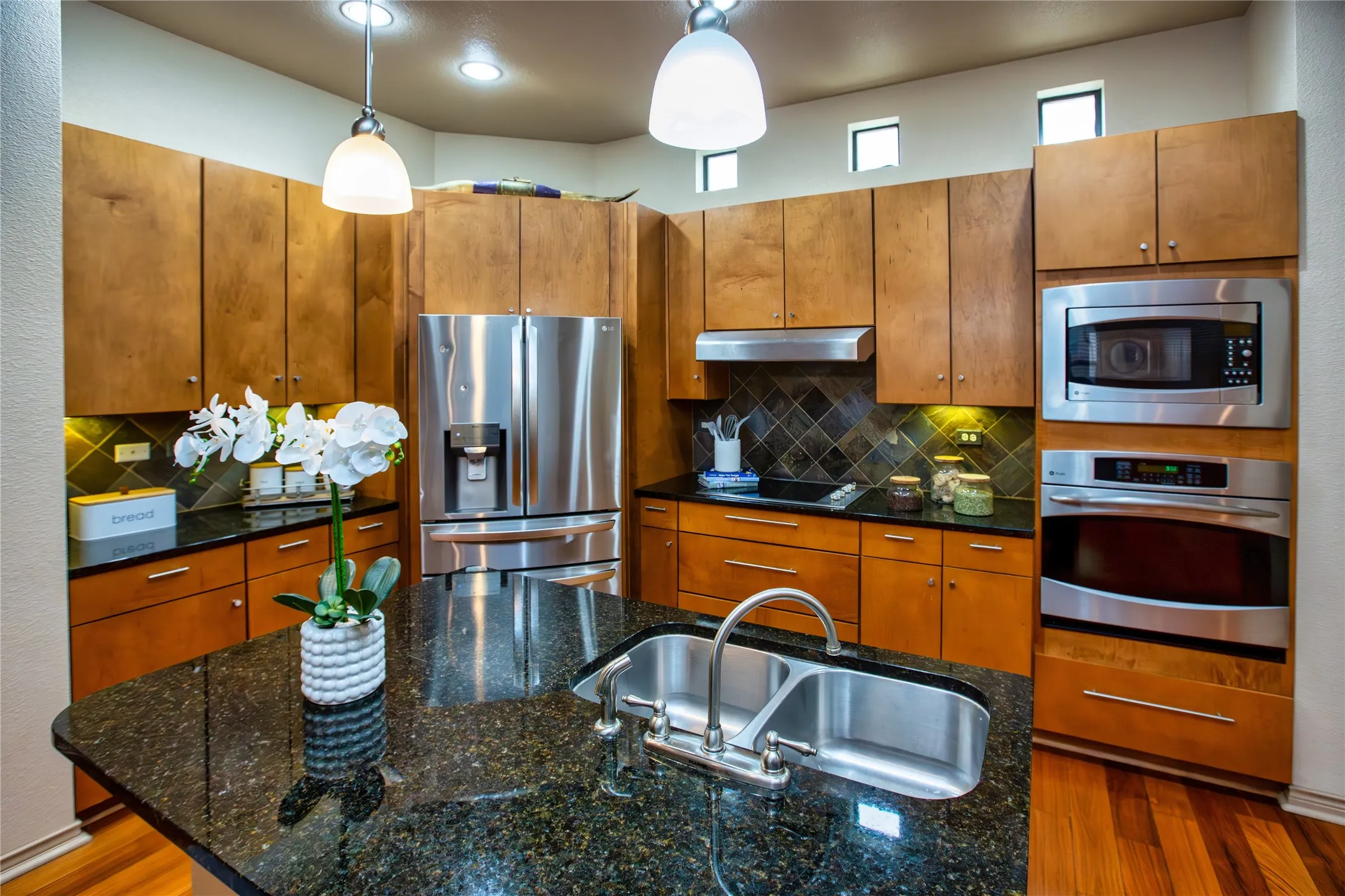 2nd Floor: Kitchen featuring stainless steel appliances, wood finish cabinetry, dark stone counters, backsplash, and decorative light fixtures
