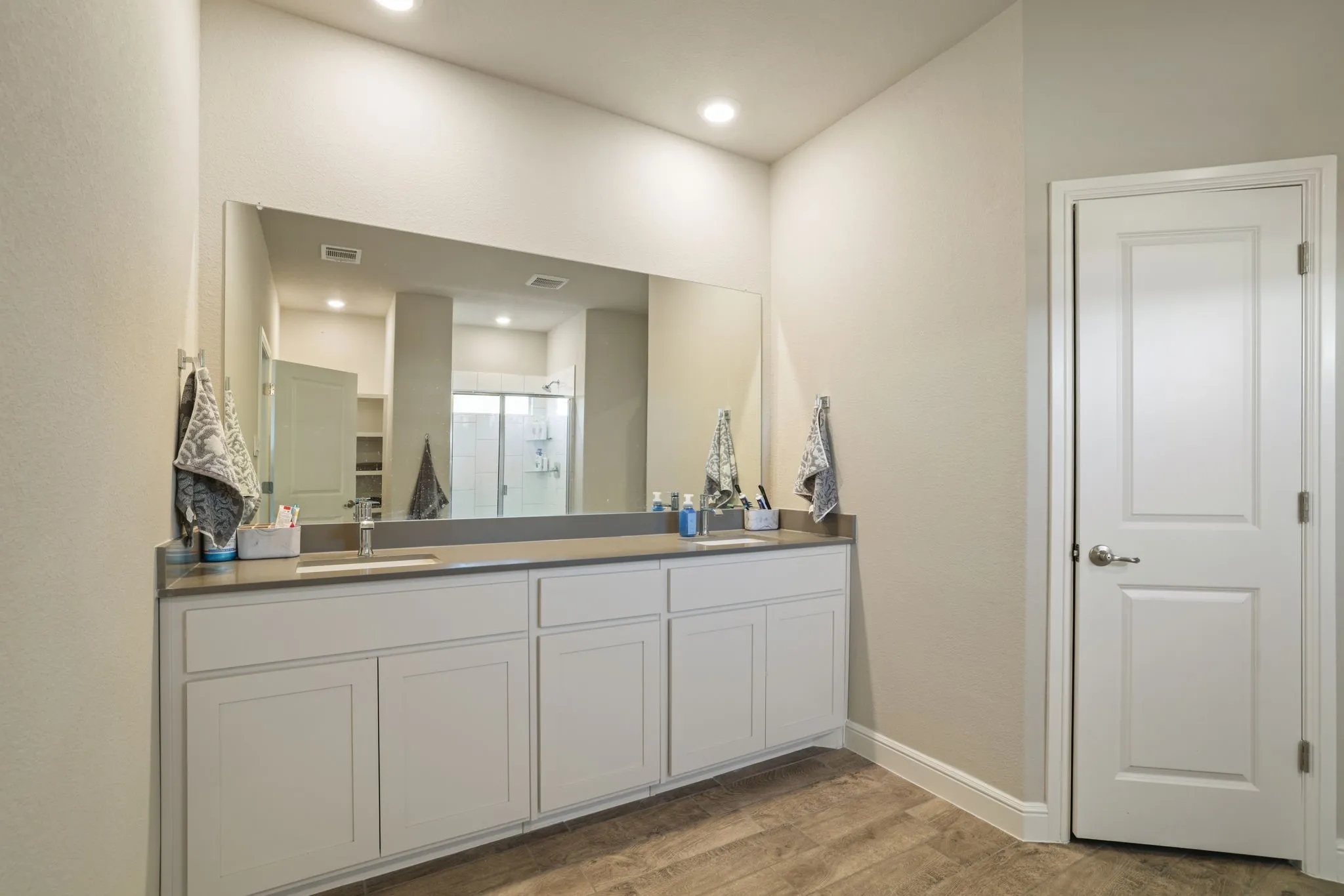 Full bath featuring a shower stall, double vanity, light wood-type flooring, and a walk in closet