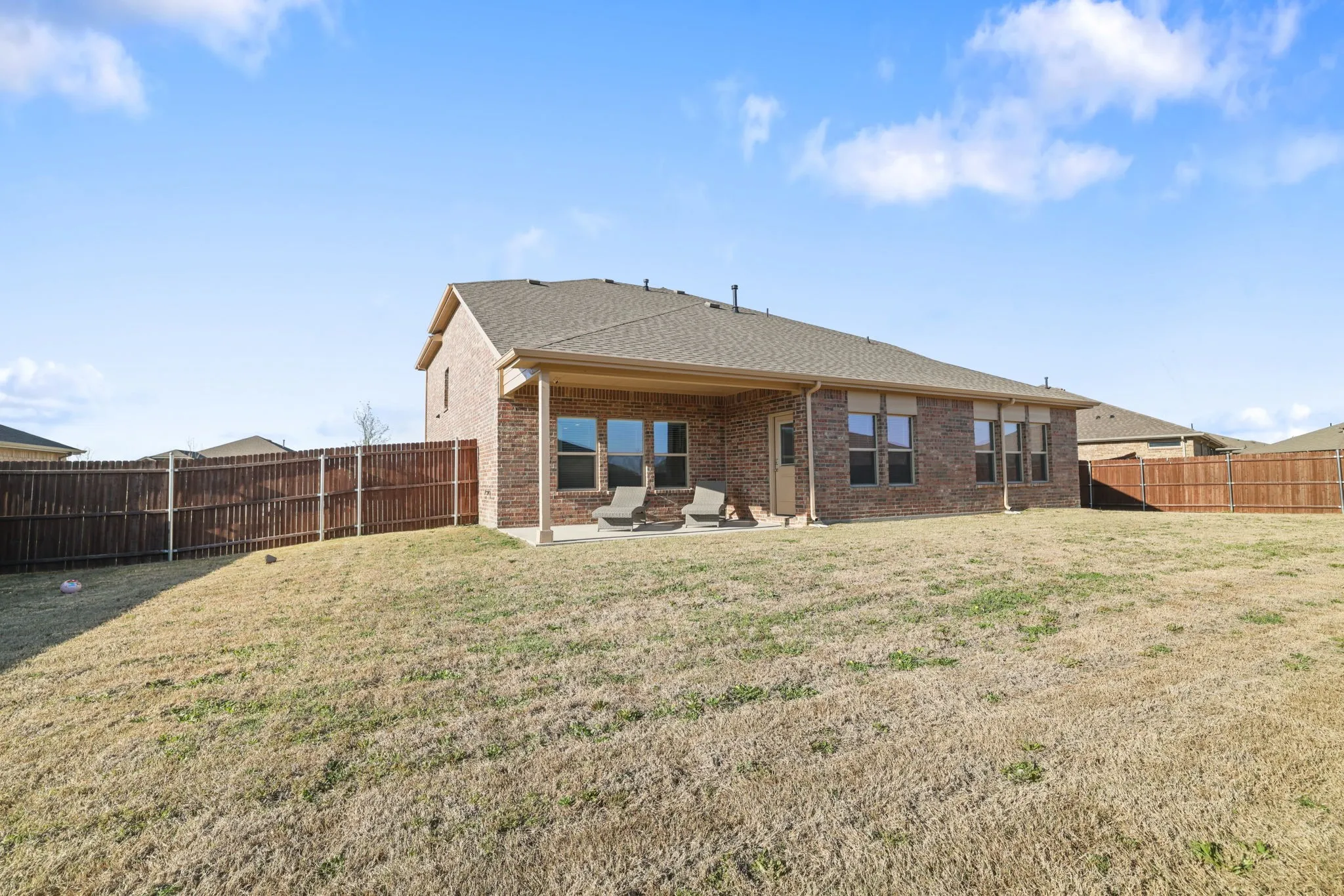 Rear view of house with a patio area, brick siding, a fenced backyard, and a shingled roof