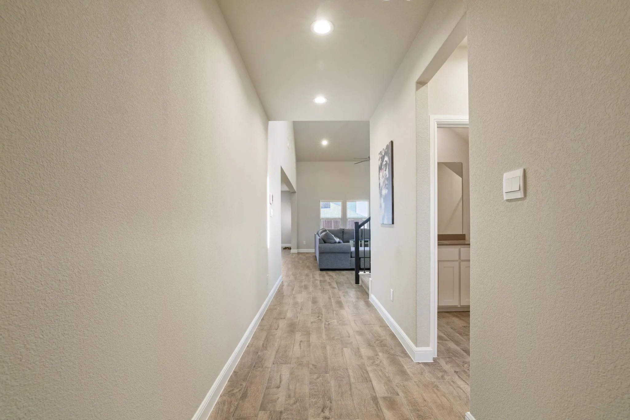 Hallway with a textured wall, light wood finished floors, and recessed lighting