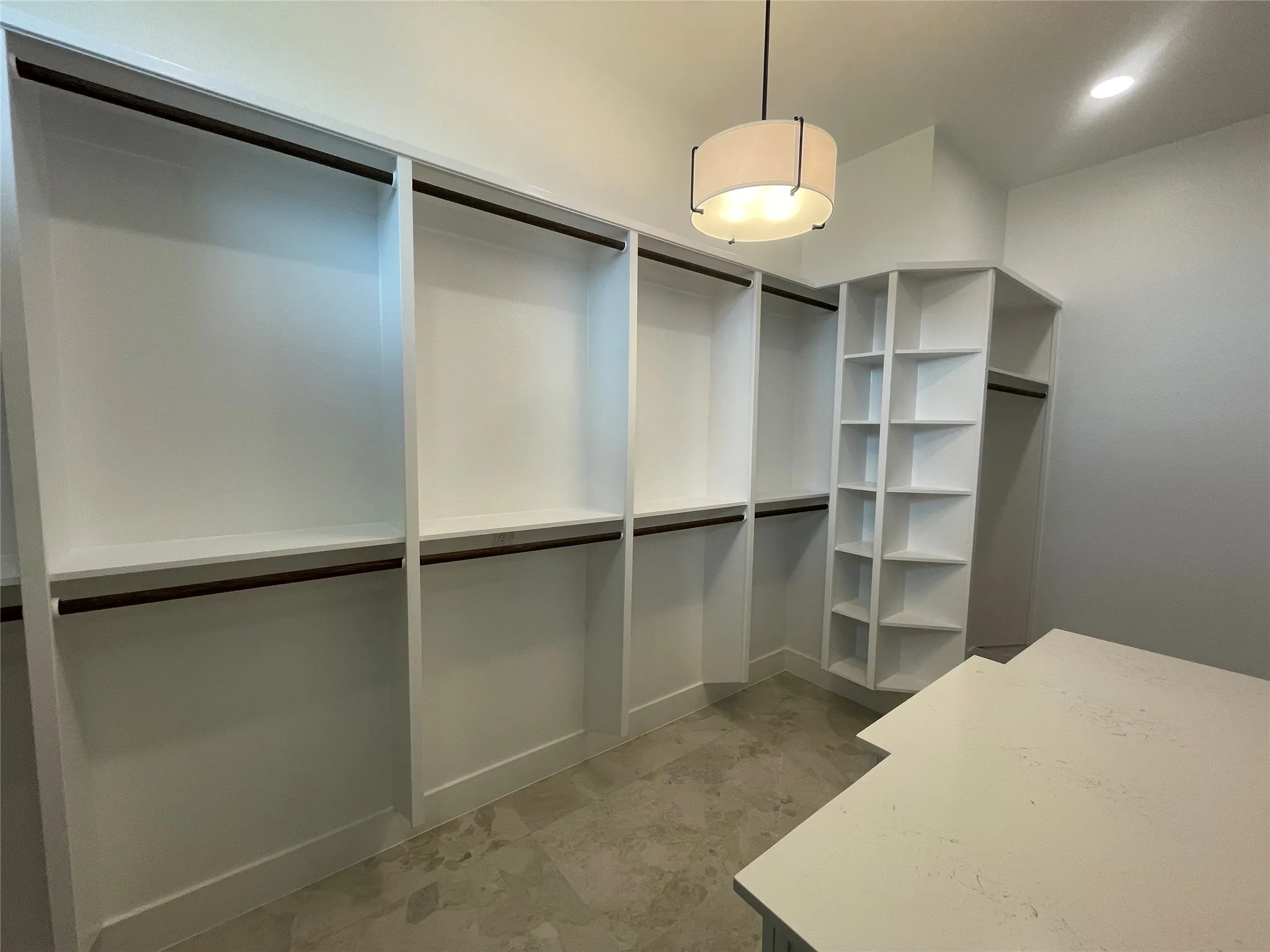 Spacious walk-in closet featuring custom built-in shelving, hanging rods, and a central island with a light-colored countertop