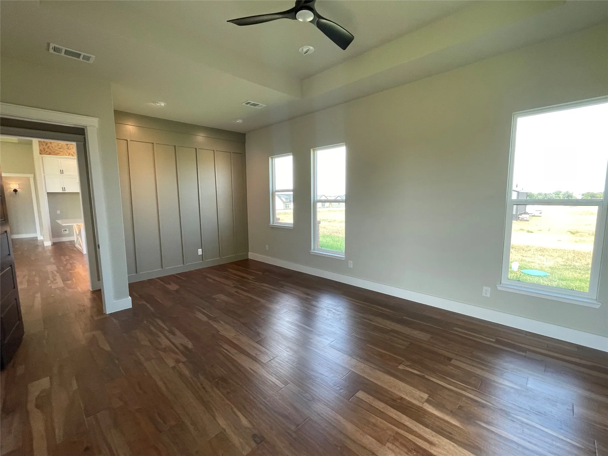 Tray ceiling with a ceiling fan, accent wall with panel detailing, wood-finish flooring, and multiple windows
