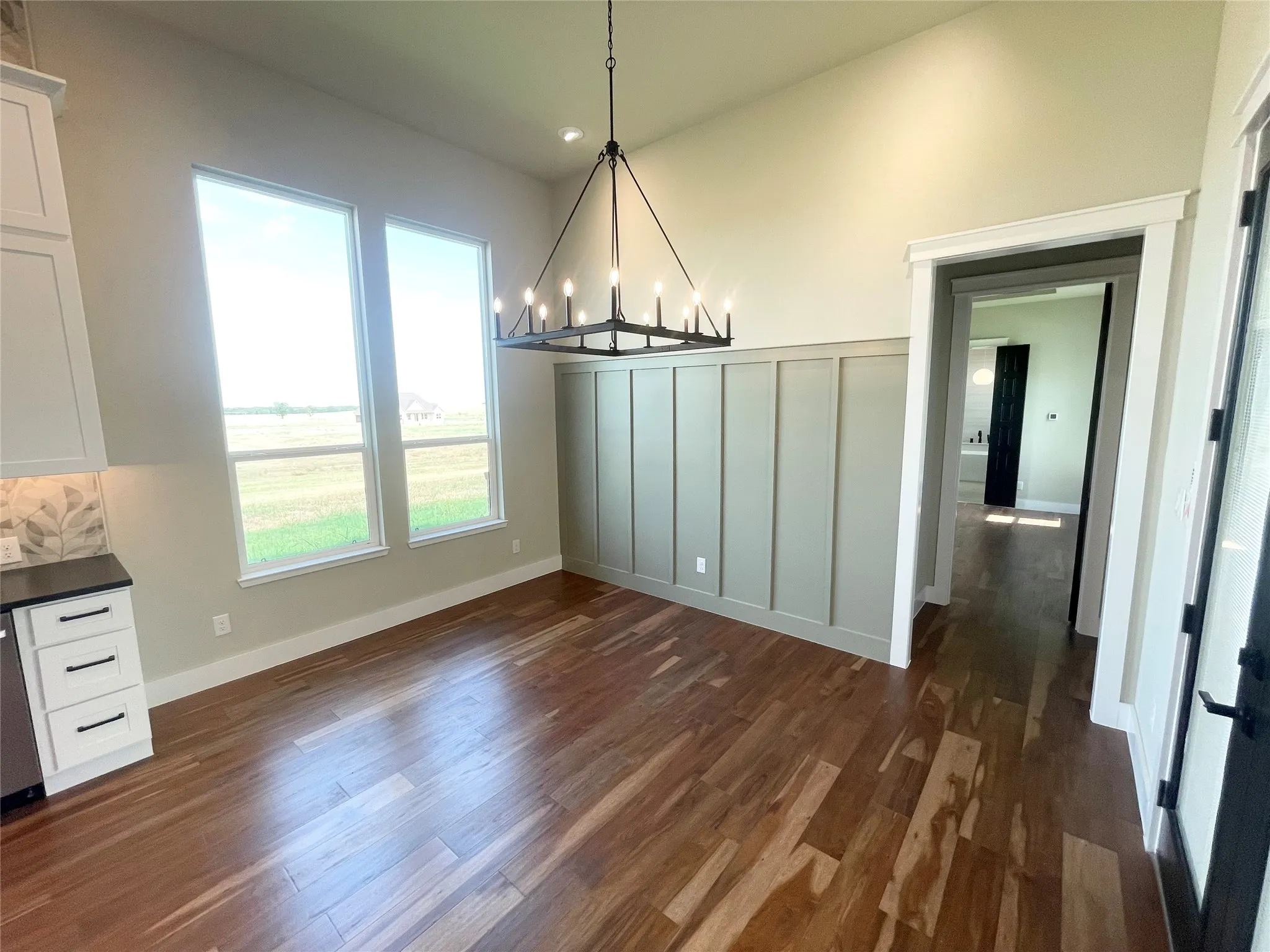 Wood-finish flooring, board and batten accent wall, dual tall windows, contemporary chandelier, and high ceilings