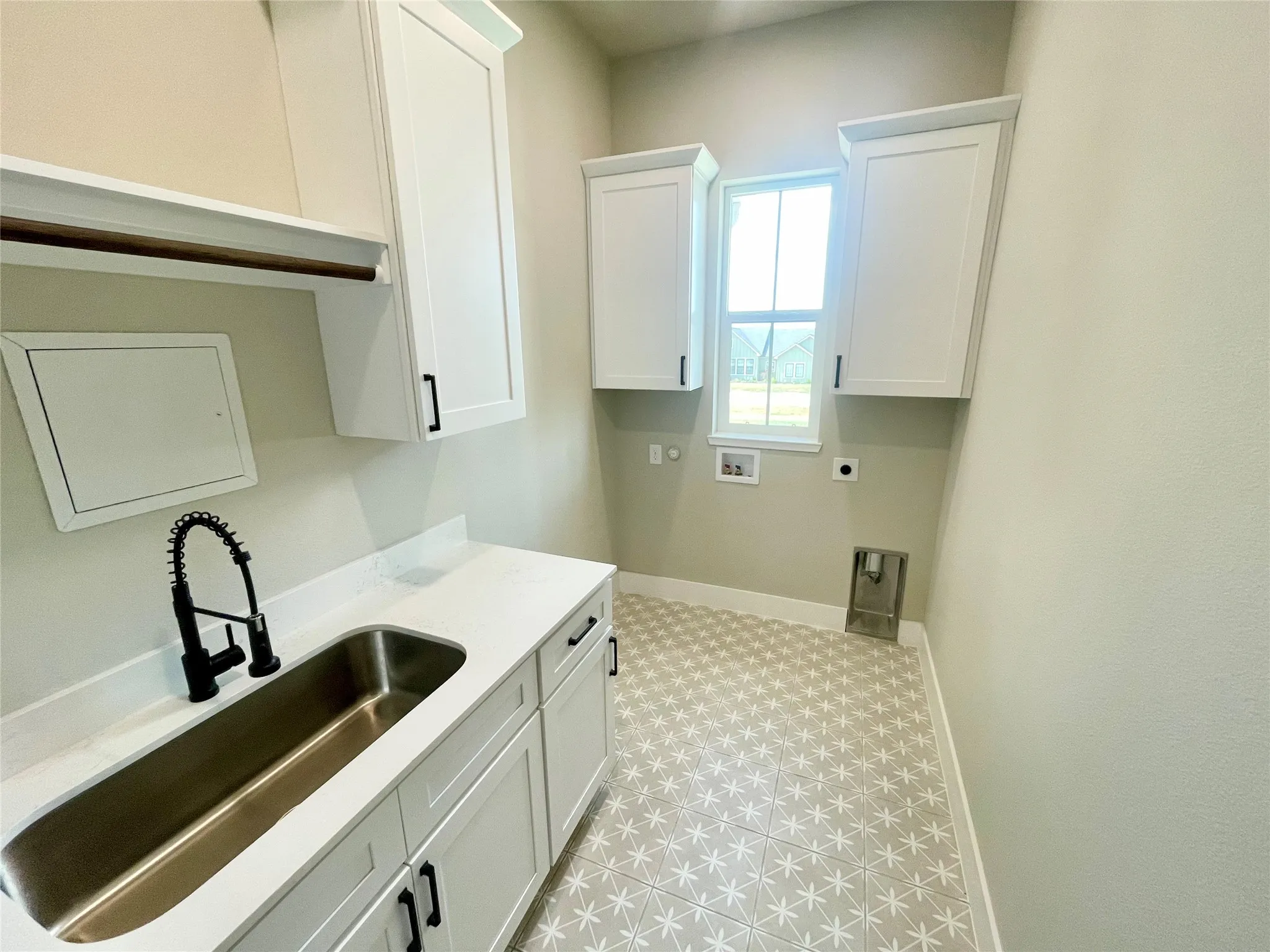 White cabinetry with black hardware, extended countertop with integrated sink, patterned floor tiles, and a window for natural light