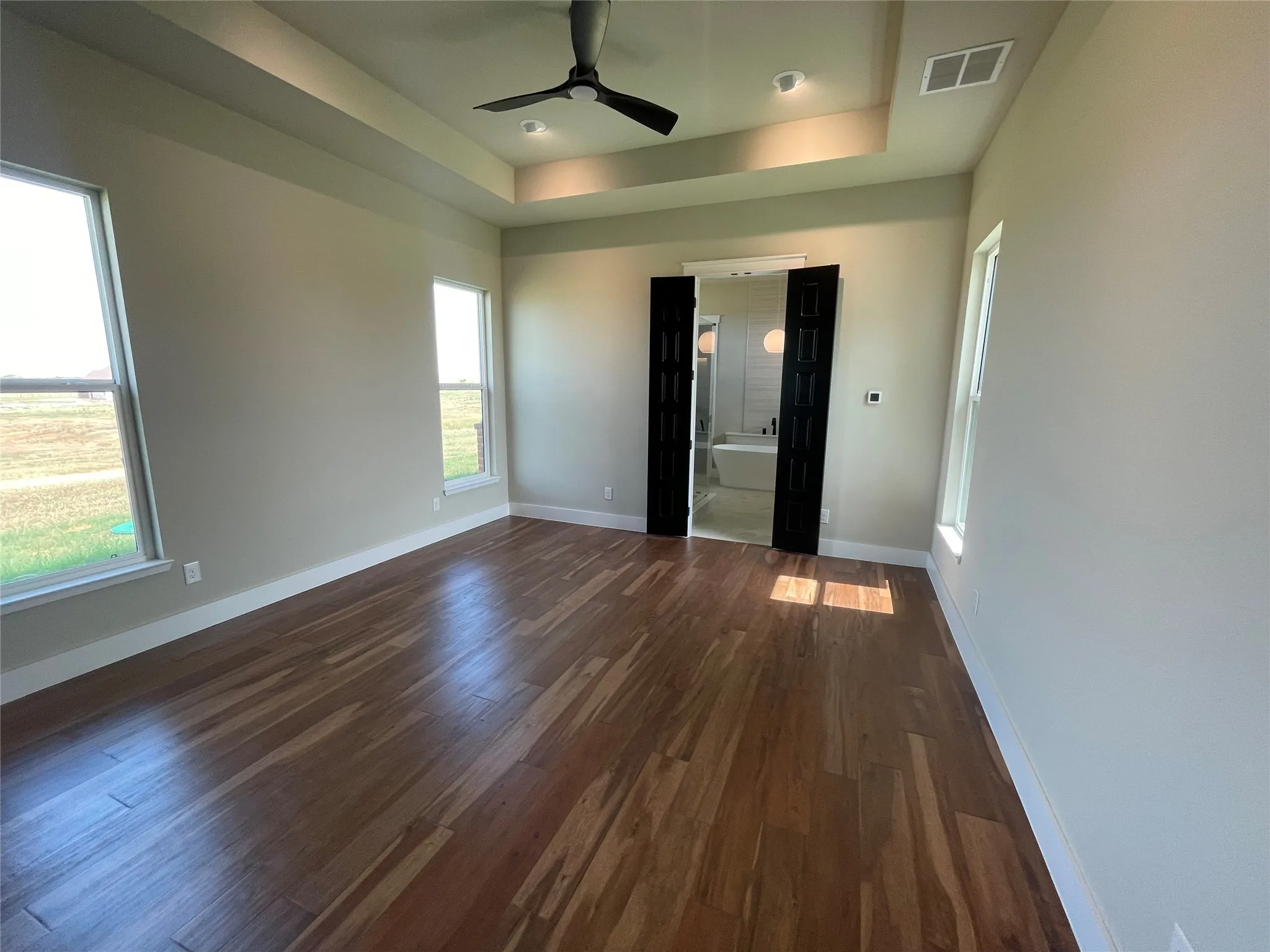 Tray ceiling with recessed lighting, wood-finish flooring, and multiple windows