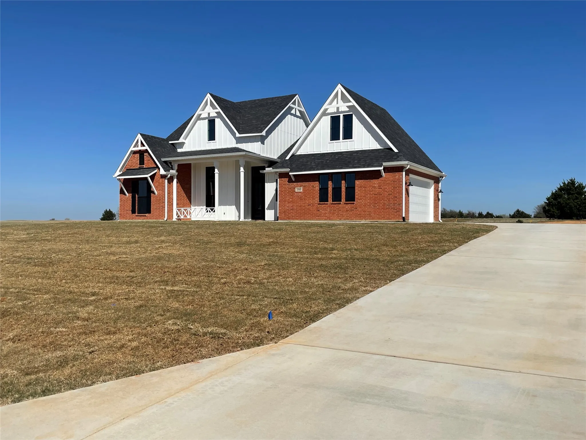 Modern farmhouse with brick siding, a front lawn, a porch, concrete driveway, and an attached garage