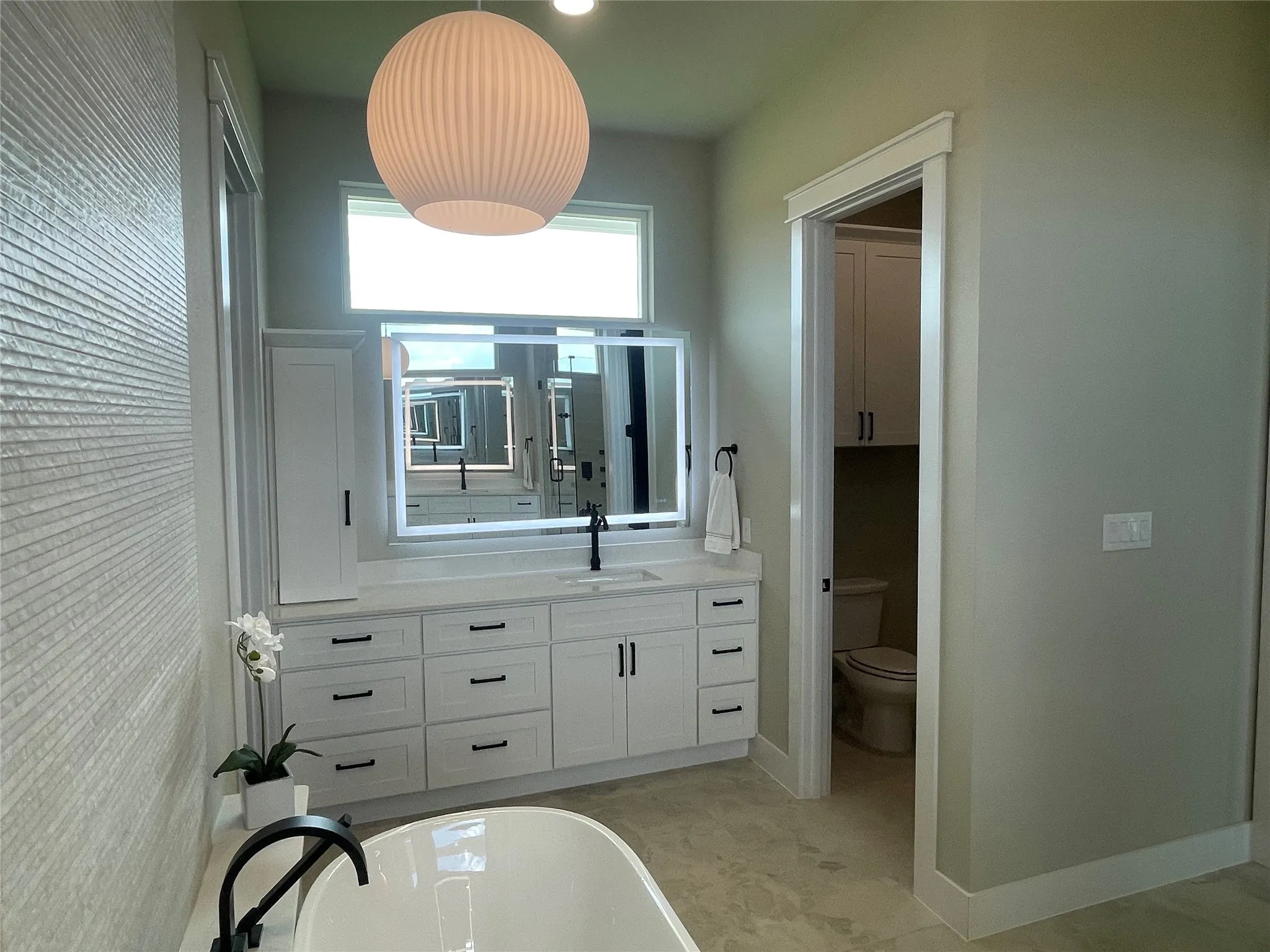 Built-in soaking tub with matte black faucet, custom vanity with undermount sink, quartz countertop, and illuminated mirror