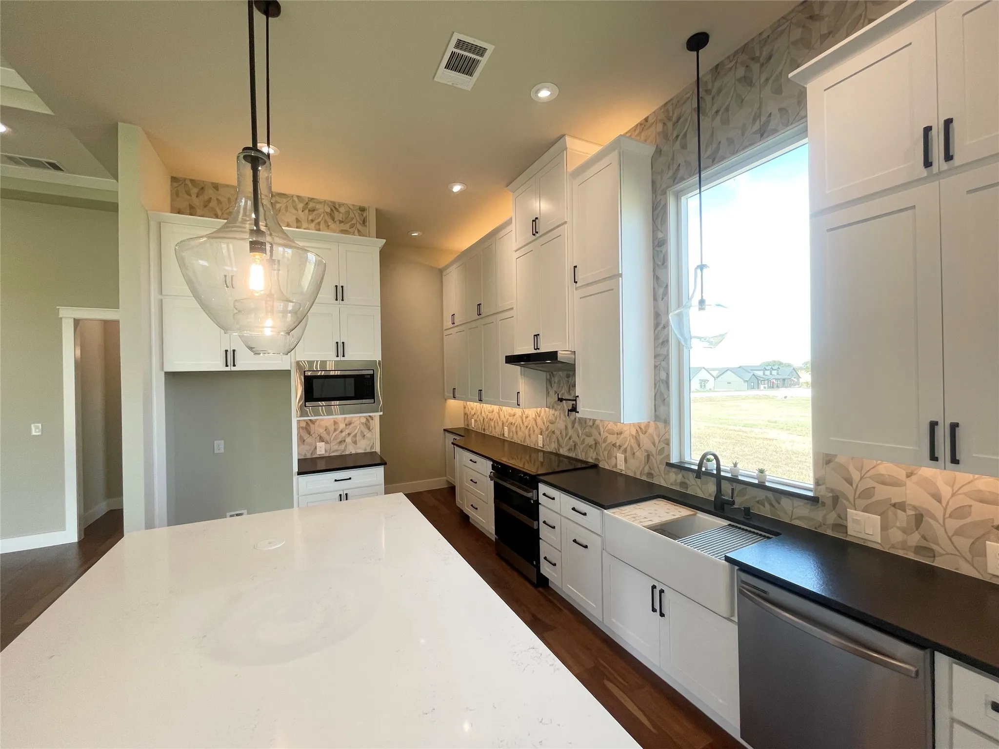 Kitchen featuring white shaker-style cabinetry, a large center island with a light-toned countertop, a farmhouse sink, stainless steel appliances, and wood-finish flooring