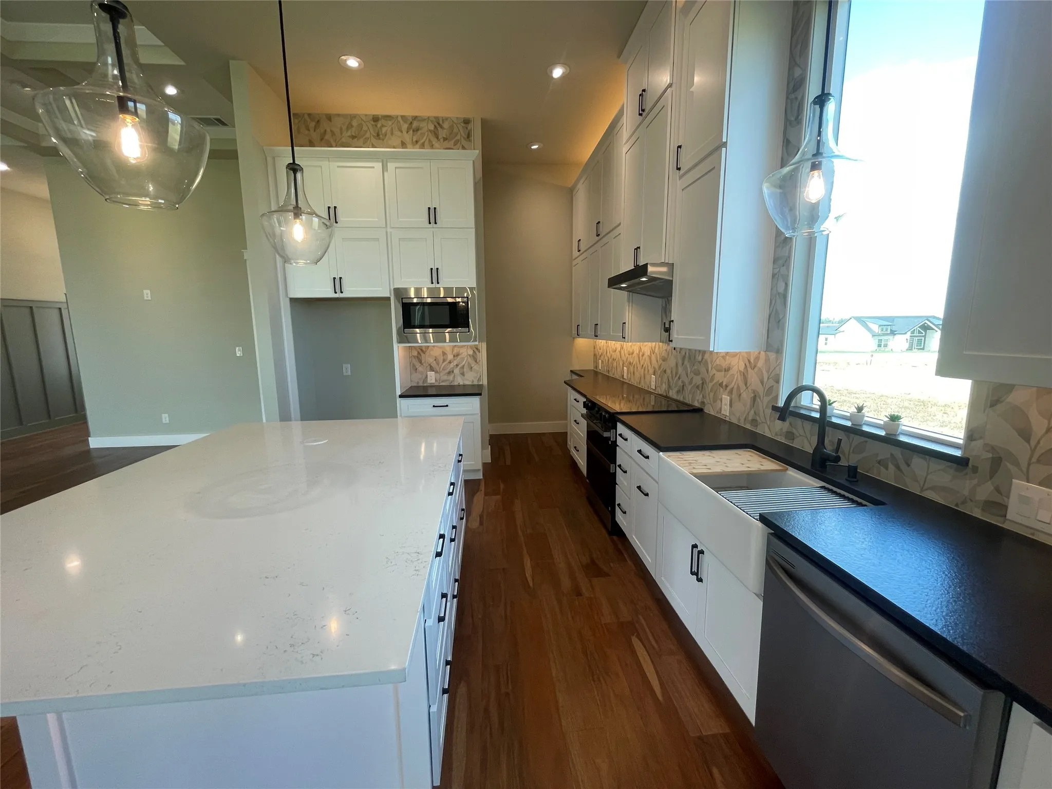 White shaker cabinetry paired with dark countertops, a large center island with a light-colored surface, and wood-finish flooring