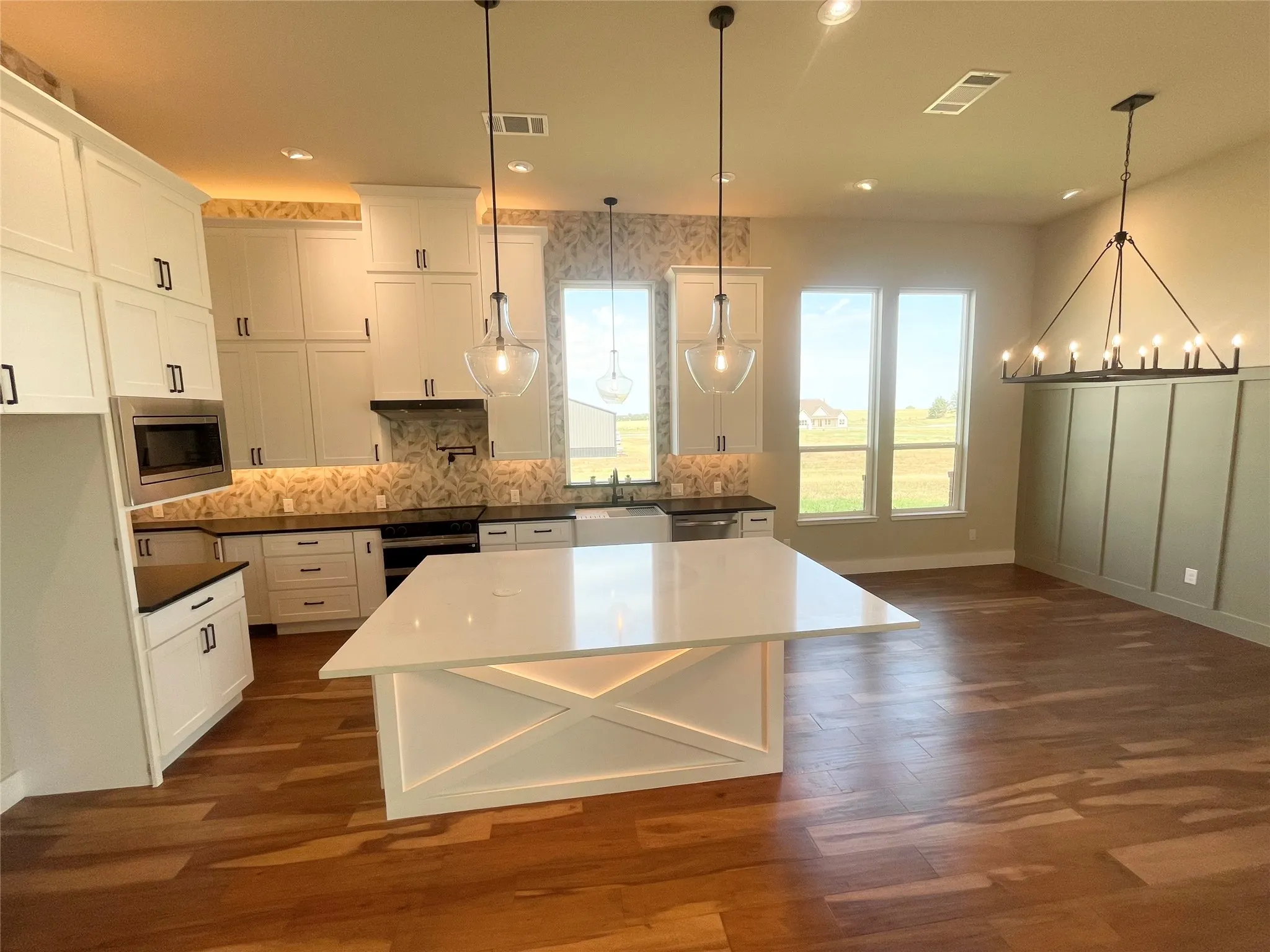 Spacious kitchen featuring white cabinetry, quartz countertops, a large island, stainless steel appliances, and wood-finish flooring