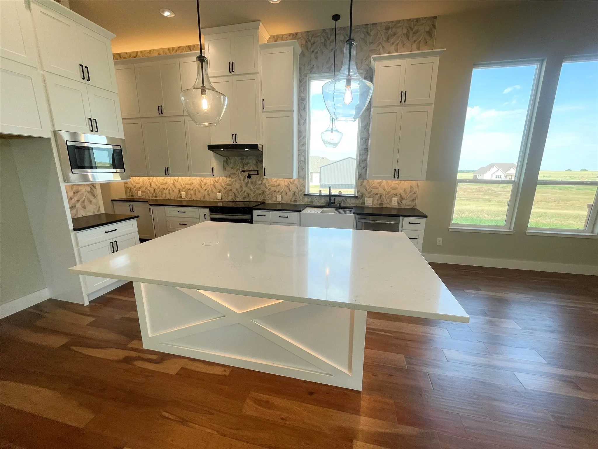 Kitchen featuring a large central island with a solid surface countertop, wood-finish flooring, white cabinetry with dark hardware, a patterned tile backsplash, and large windows
