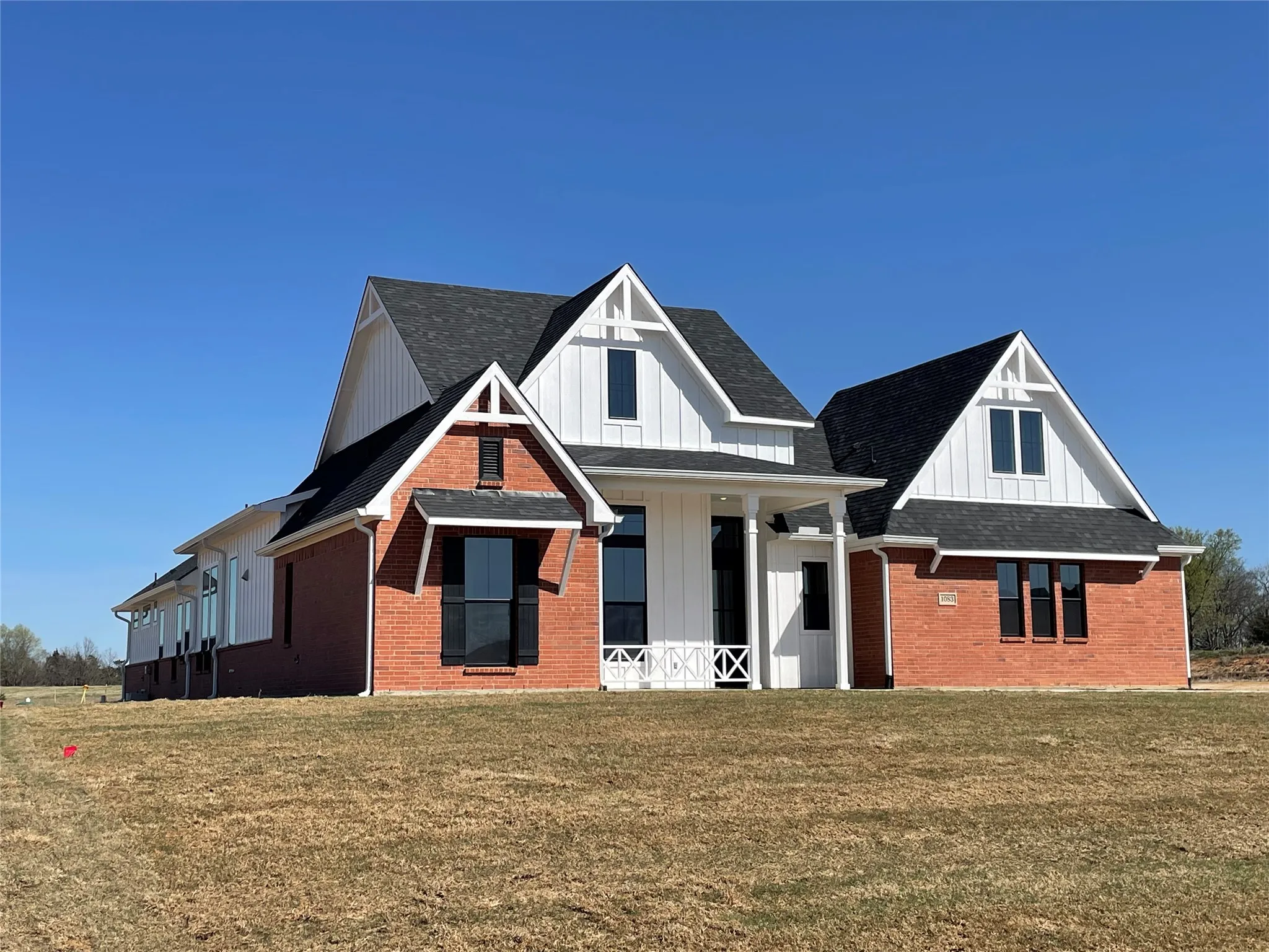 Modern farmhouse featuring board and batten siding, brick siding, a porch, and a front lawn