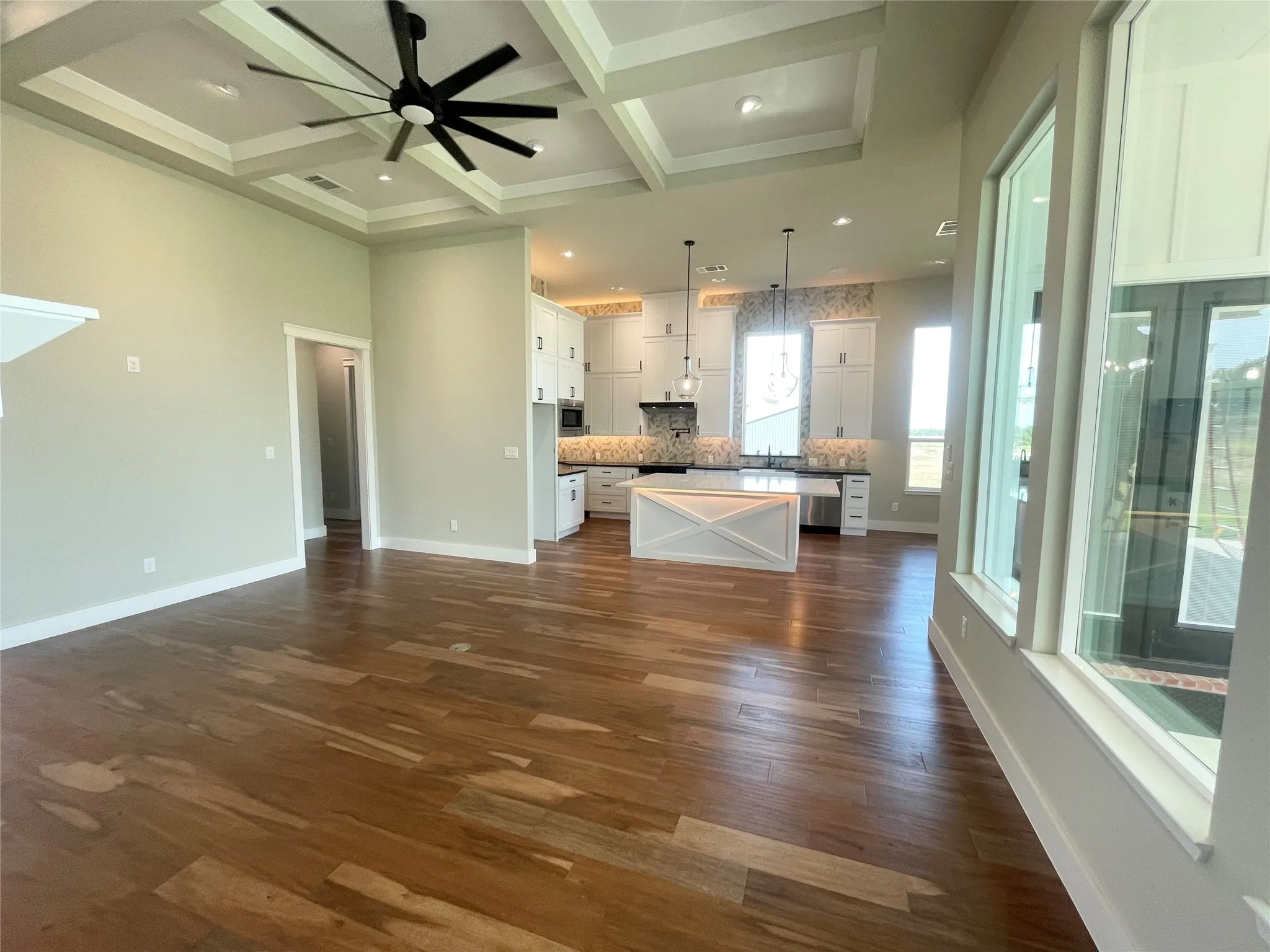 Hardwood-finish flooring, coffered ceiling with a ceiling fan, recessed lighting, white cabinetry, and a kitchen island with a light-toned countertop