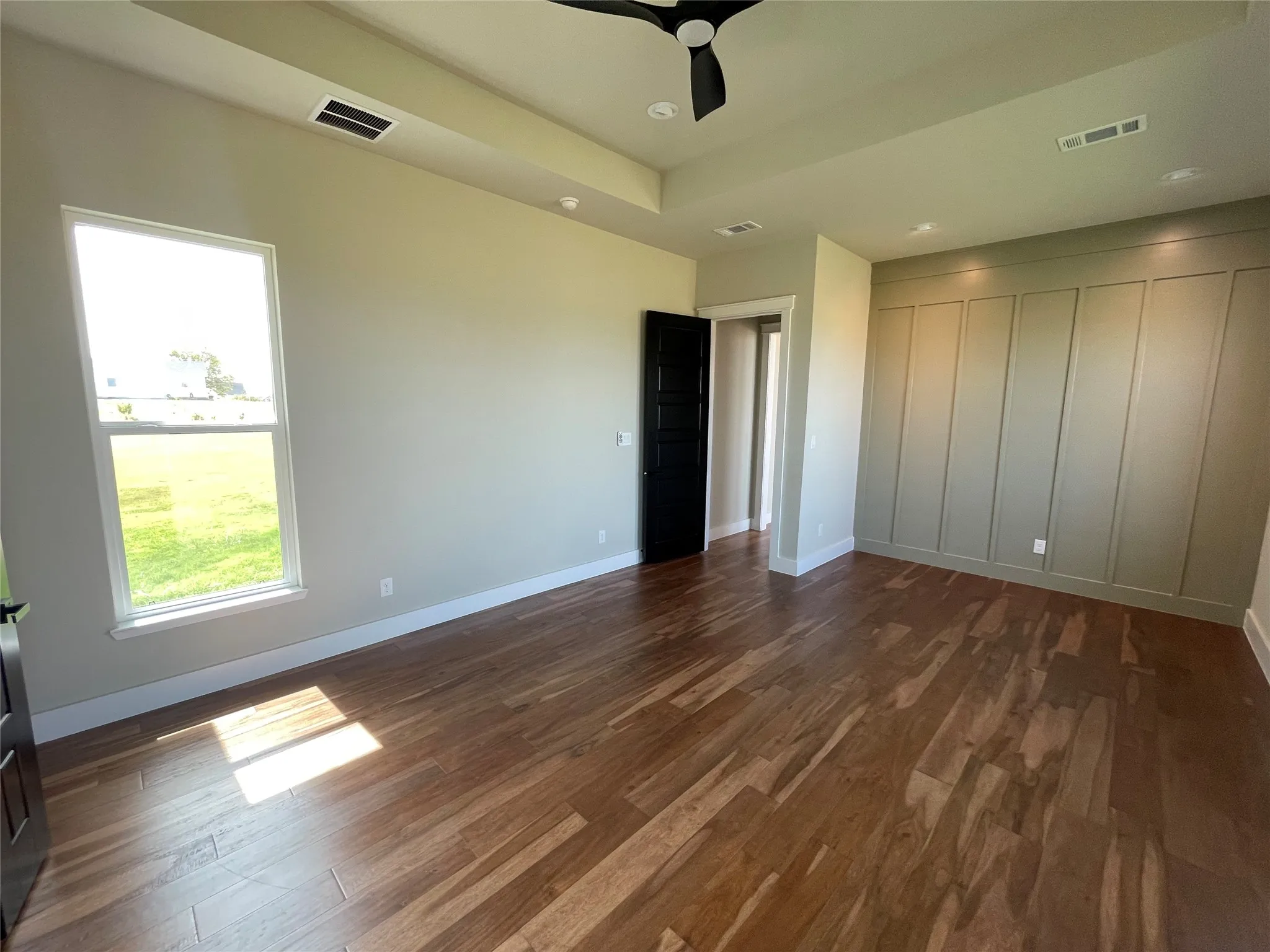 Hardwood flooring, tray ceiling, recessed lighting, accent wall with vertical paneling, and a contemporary ceiling fan
