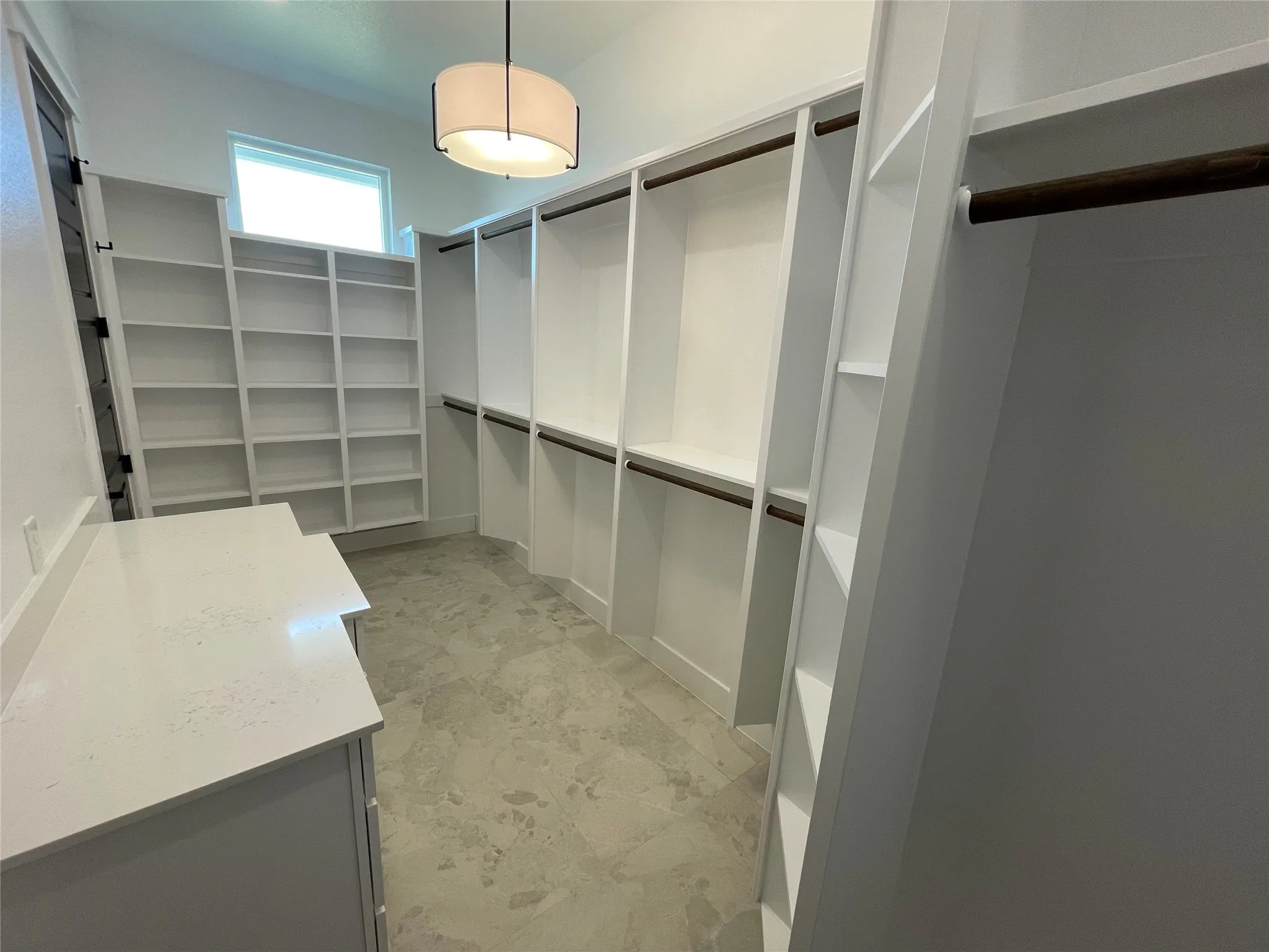 Custom built-in shelving, integrated hanging rods, window for natural light, ceiling-mounted light fixture, and floor-level storage