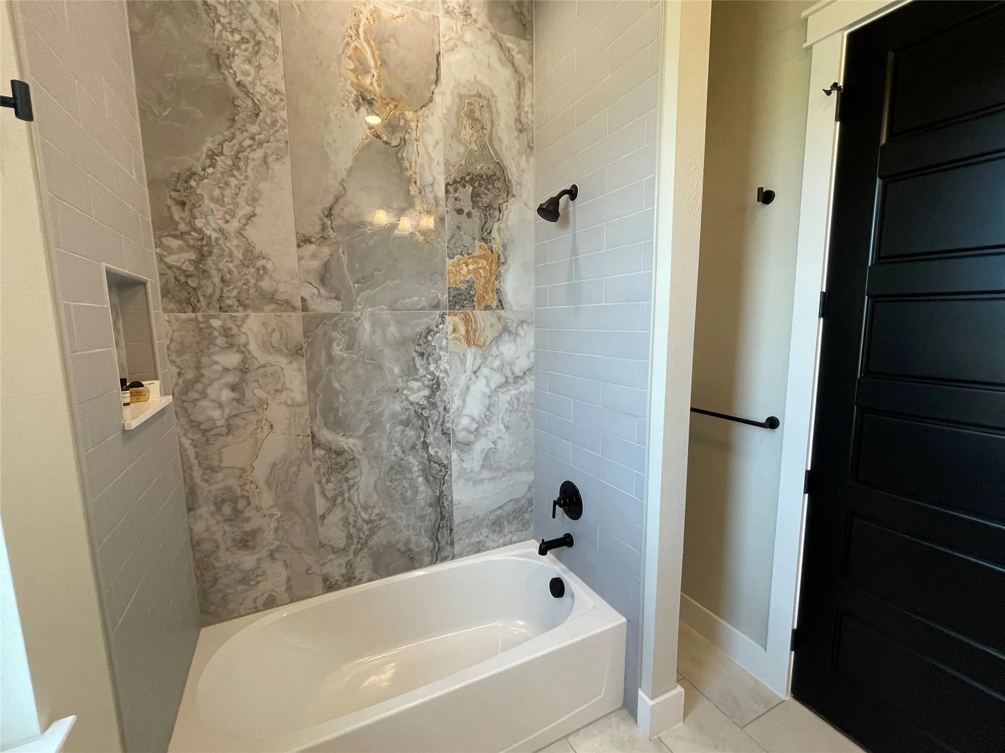 Bathtub with dark bronze fixtures, subway tile surround, recessed niche, and large format wall tiles