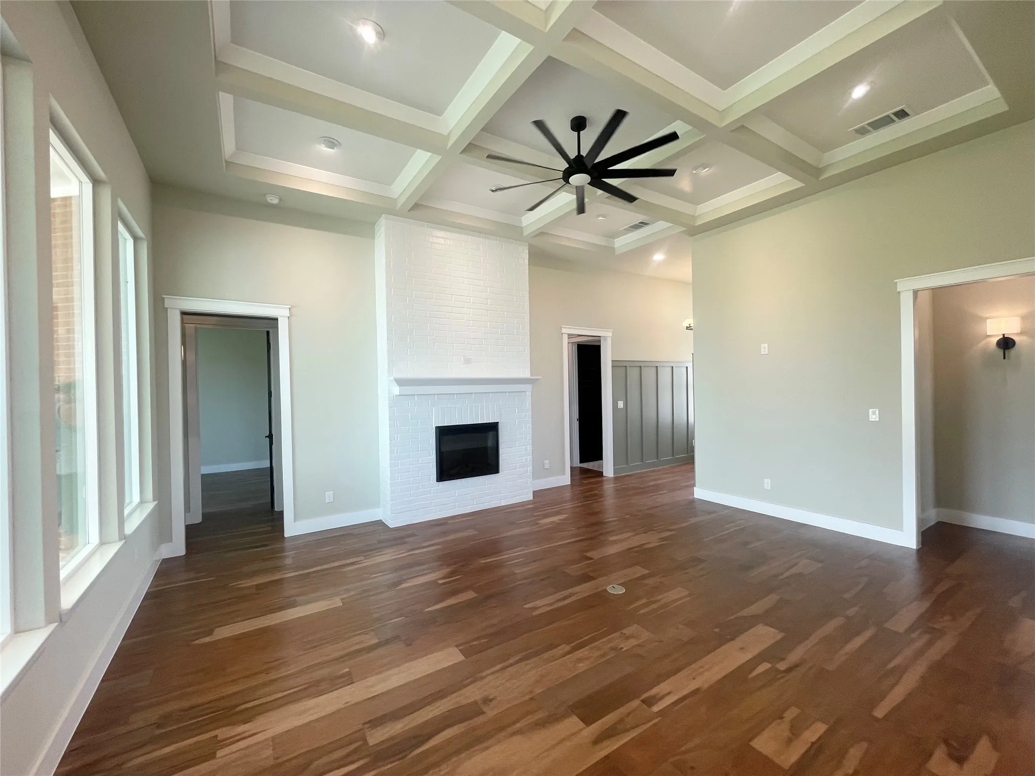 Spacious living area featuring wood-finish flooring, a white brick fireplace, and a coffered ceiling with recessed lighting