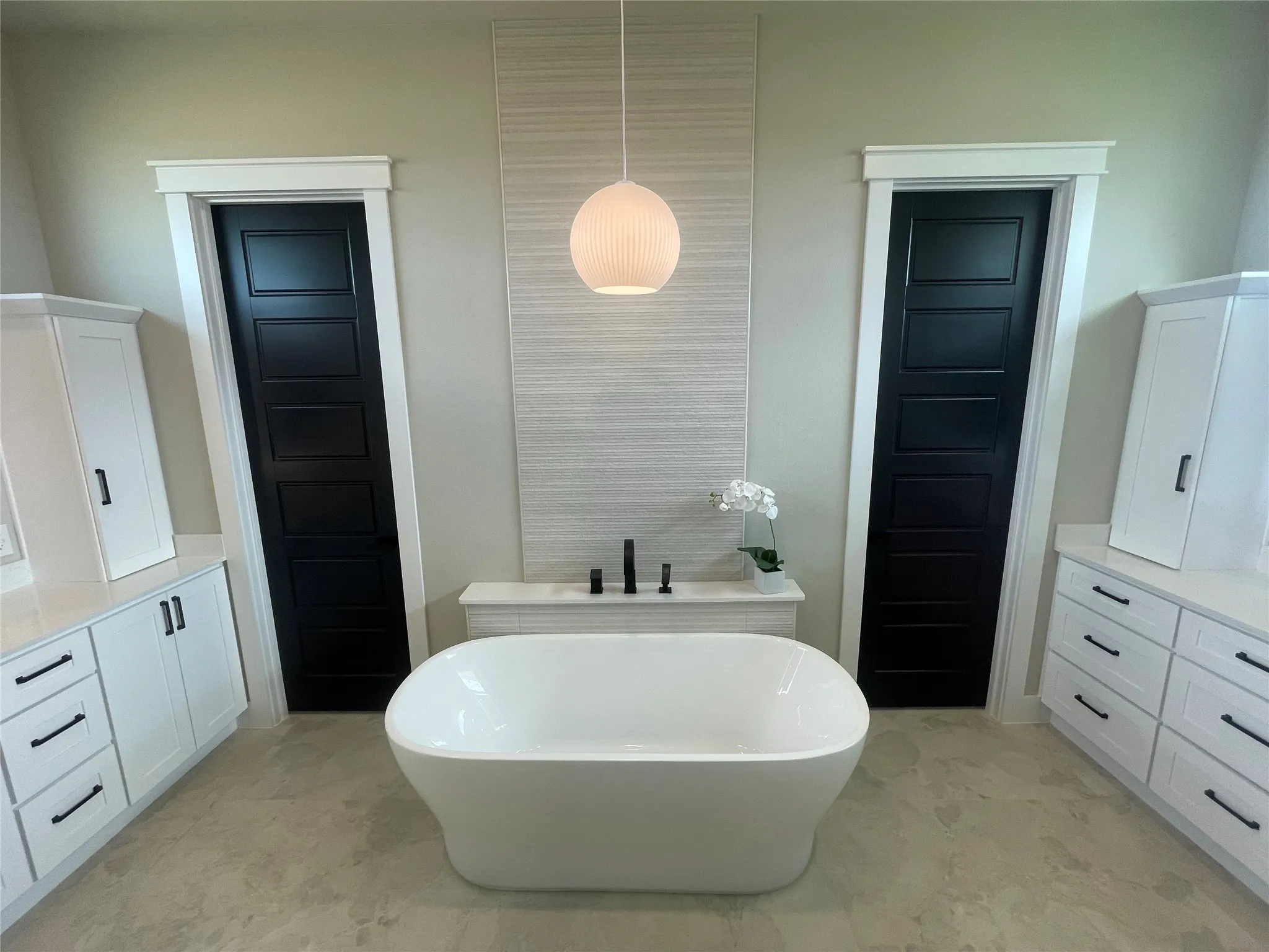 Freestanding soaking tub, dual white vanities with integrated storage, light-colored flooring, and matte black hardware