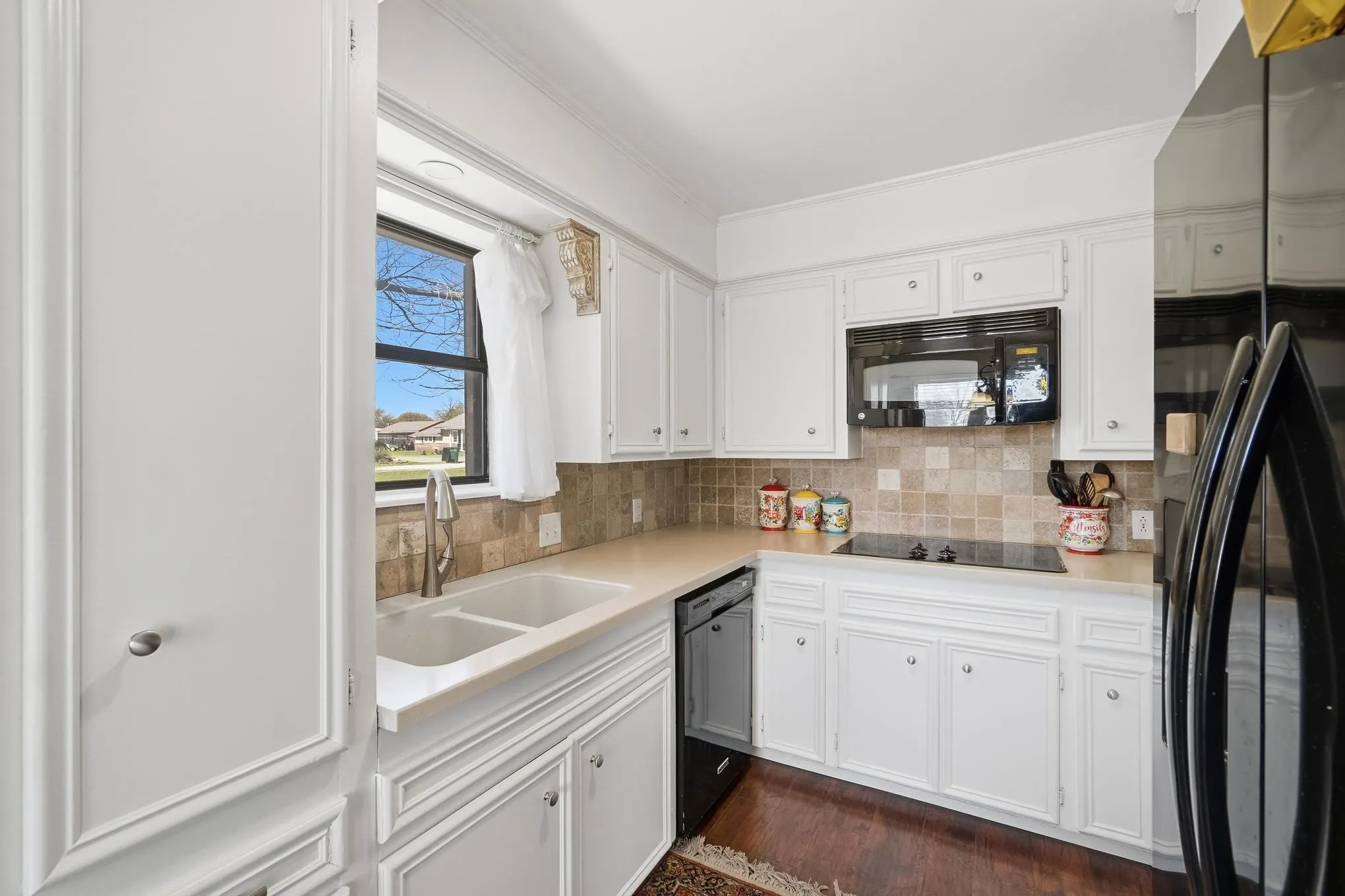 Kitchen with black appliances, white cabinets, dark wood-type flooring, and crown molding
