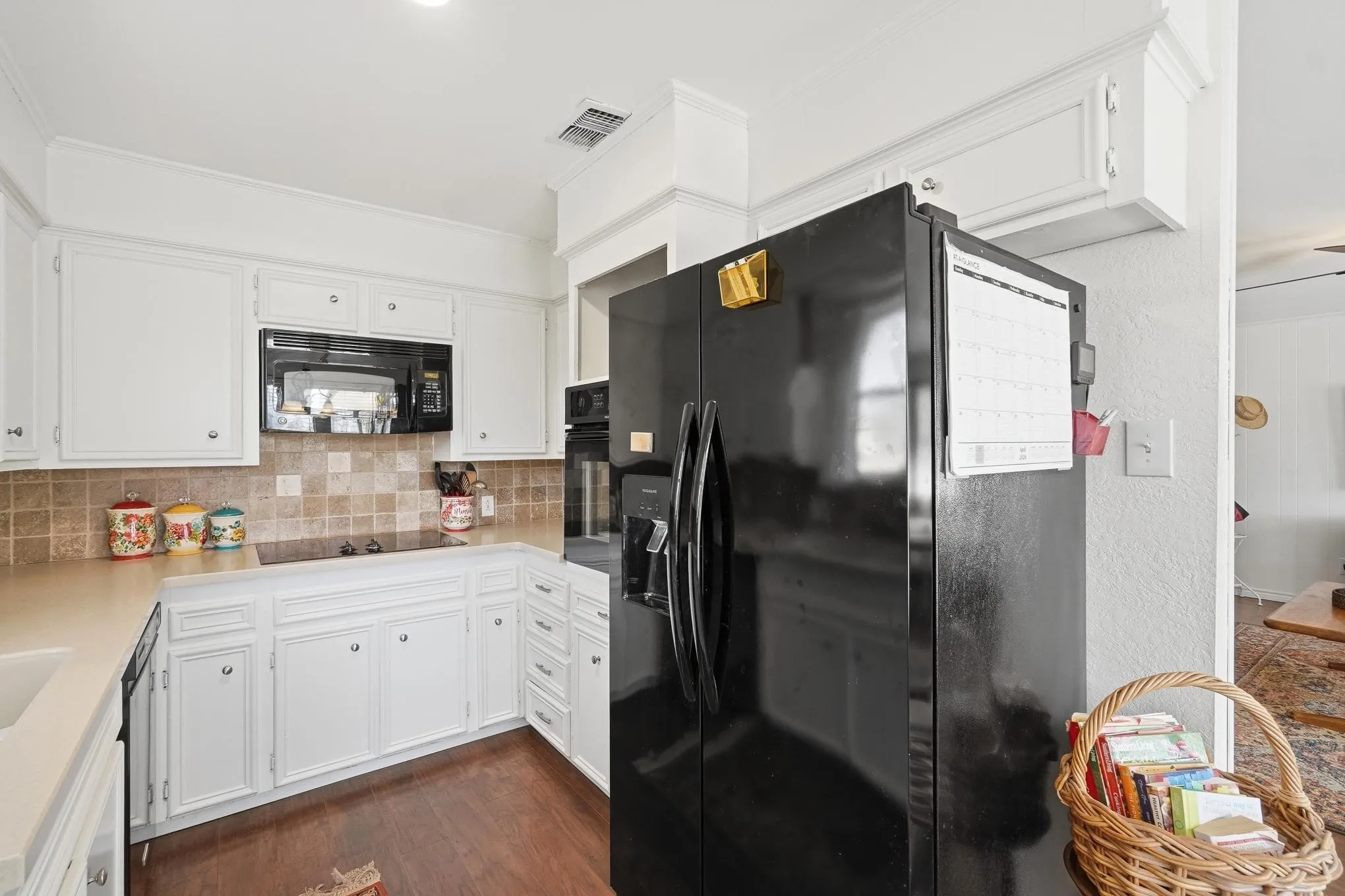 Kitchen featuring black appliances, white cabinets, dark wood finished floors, and backsplash