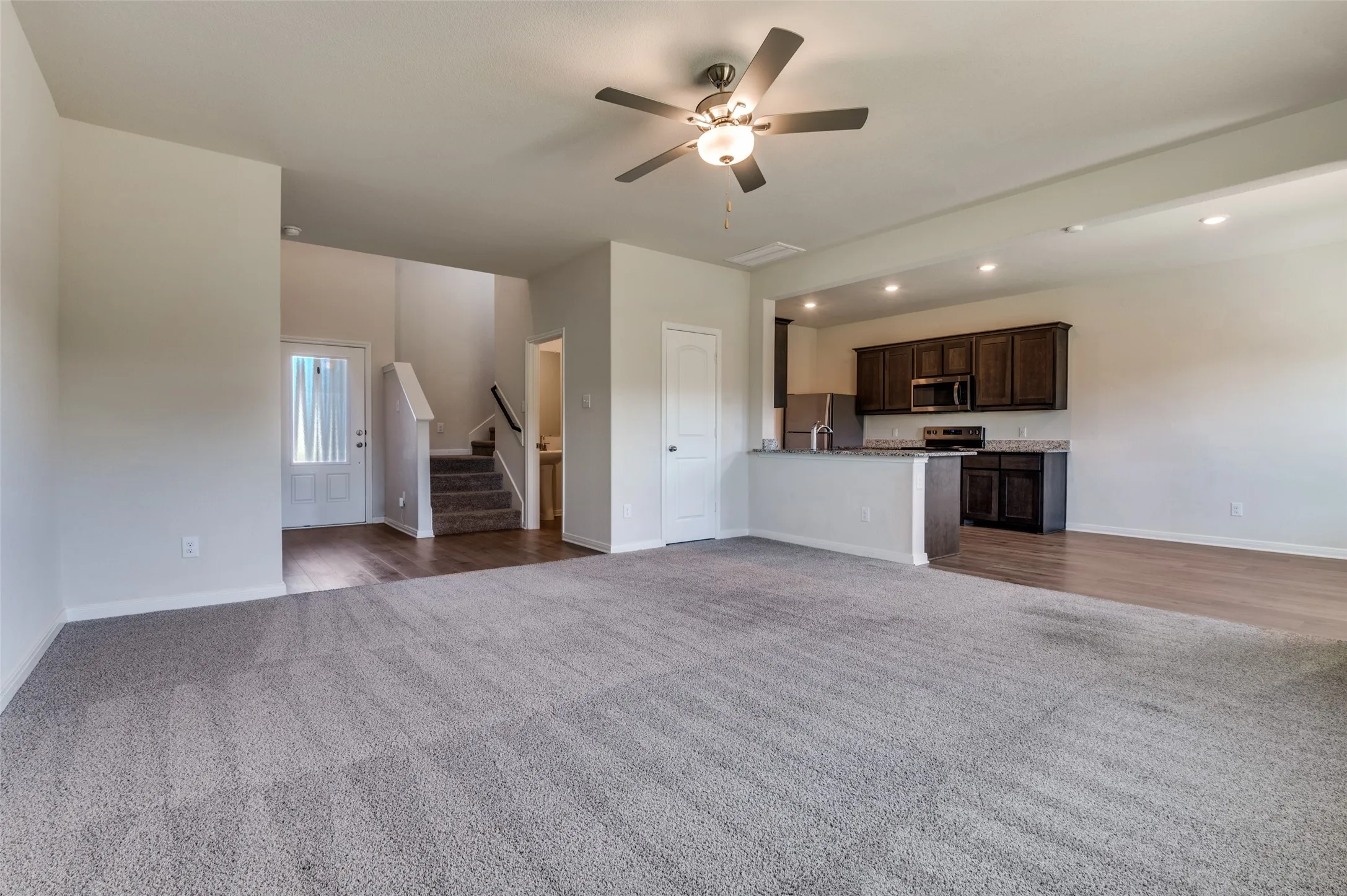 Unfurnished living room featuring dark colored carpet, ceiling fan, and recessed lighting