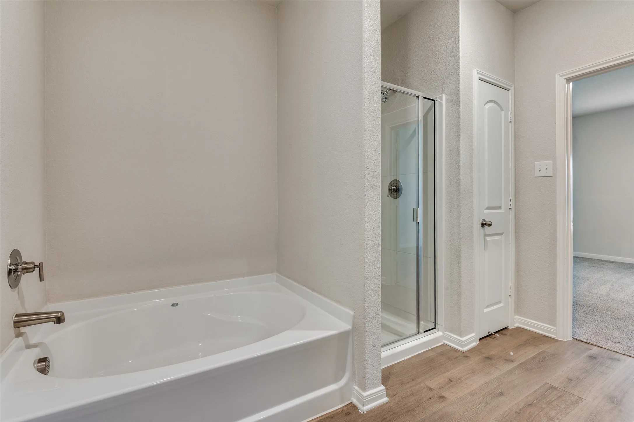 Bathroom featuring a garden tub, a shower stall, and light wood-style flooring