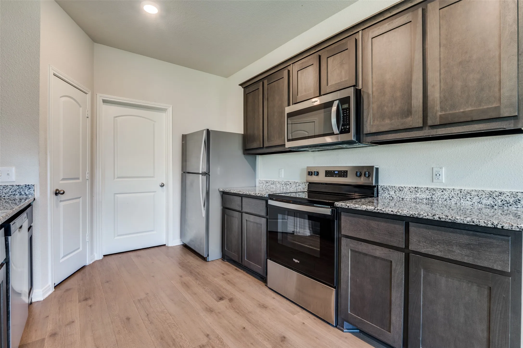 Kitchen with stainless steel appliances, light stone countertops, dark wood finish cabinetry, and light wood-type flooring