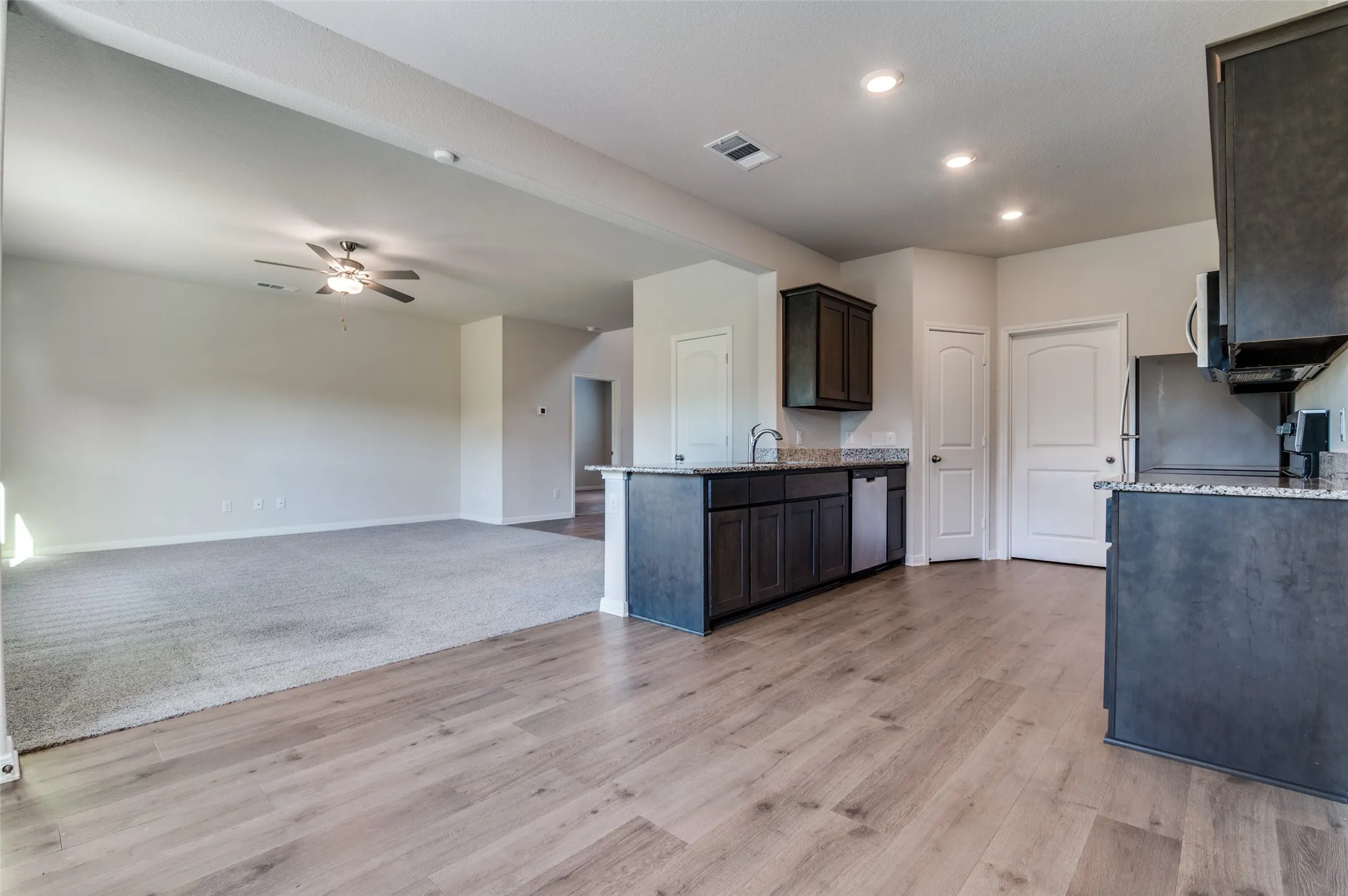 Kitchen featuring light stone countertops, open floor plan, ceiling fan, dark wood finish cabinets, and light wood-type flooring