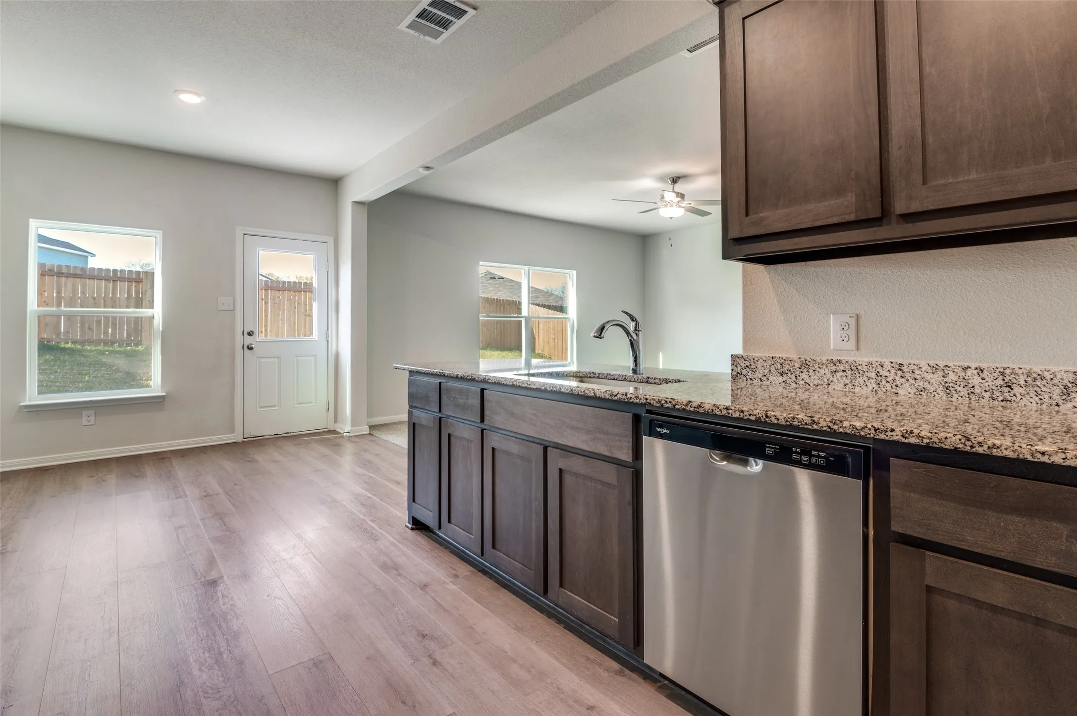 Kitchen featuring stainless steel dishwasher, a peninsula, light wood-type flooring, light stone countertops, and dark wood finish cabinetry
