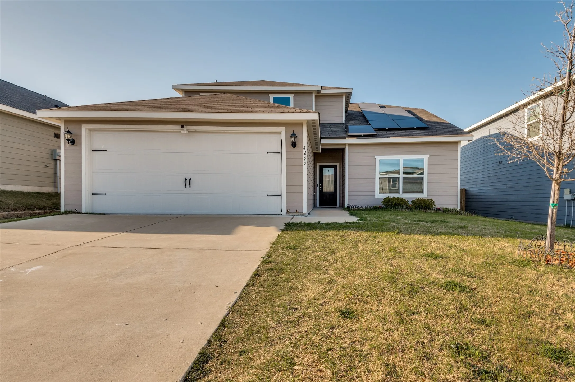 View of front facade featuring solar panels, a garage, driveway, a front yard, and roof with shingles