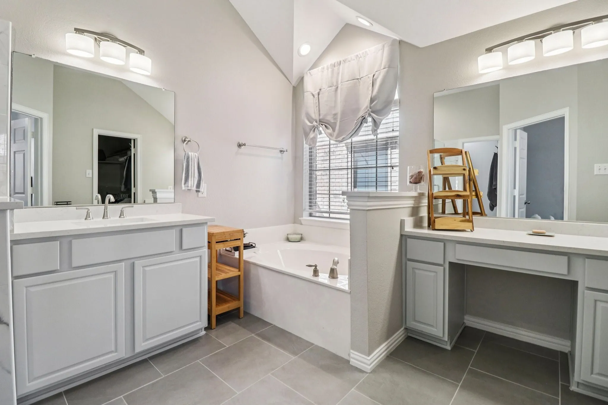 Bathroom with a garden tub, light tile patterned floors, two vanities, and vaulted ceiling