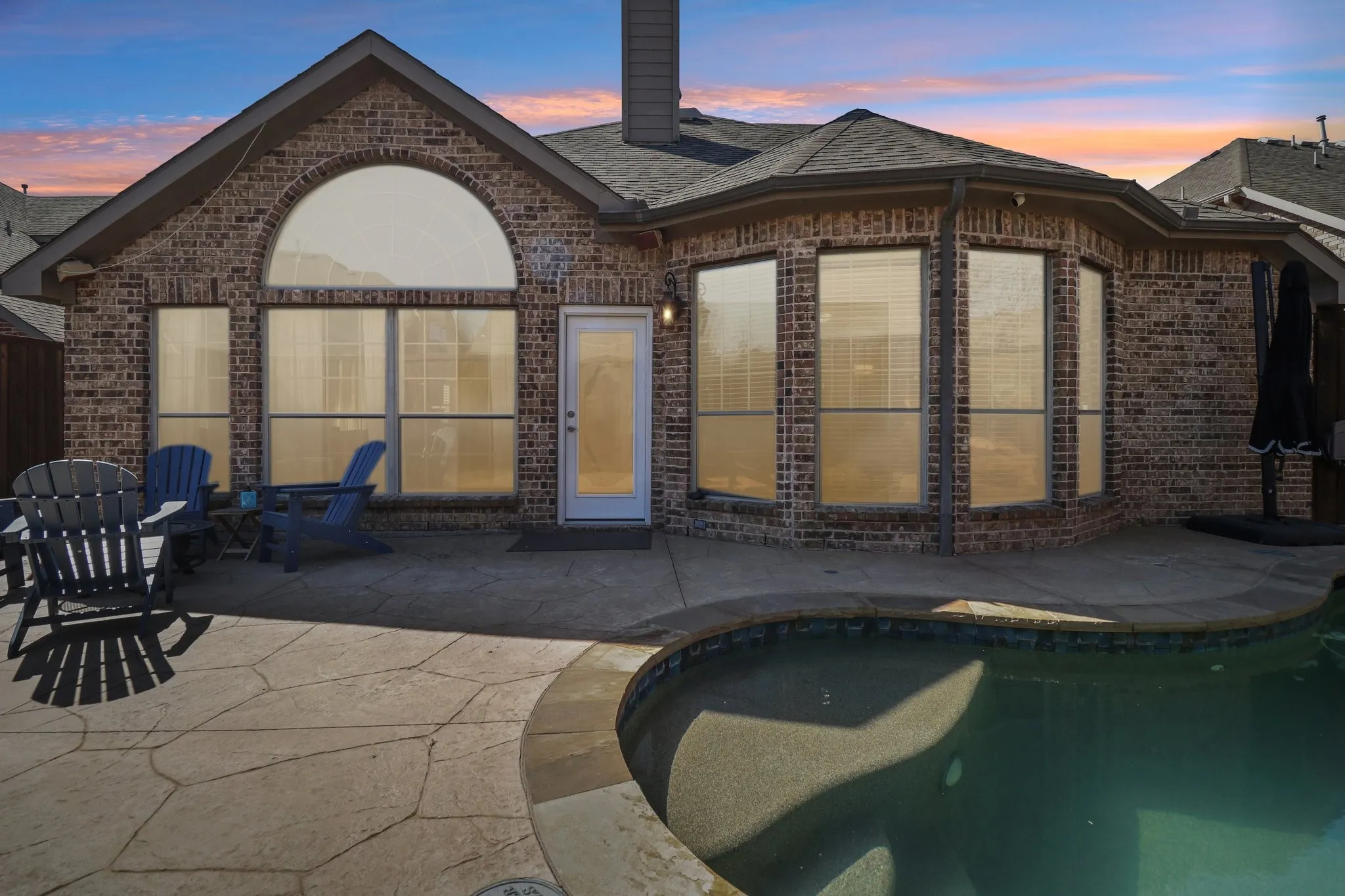 Rear view of property featuring an outdoor pool, brick siding, a patio, a chimney, and roof with shingles