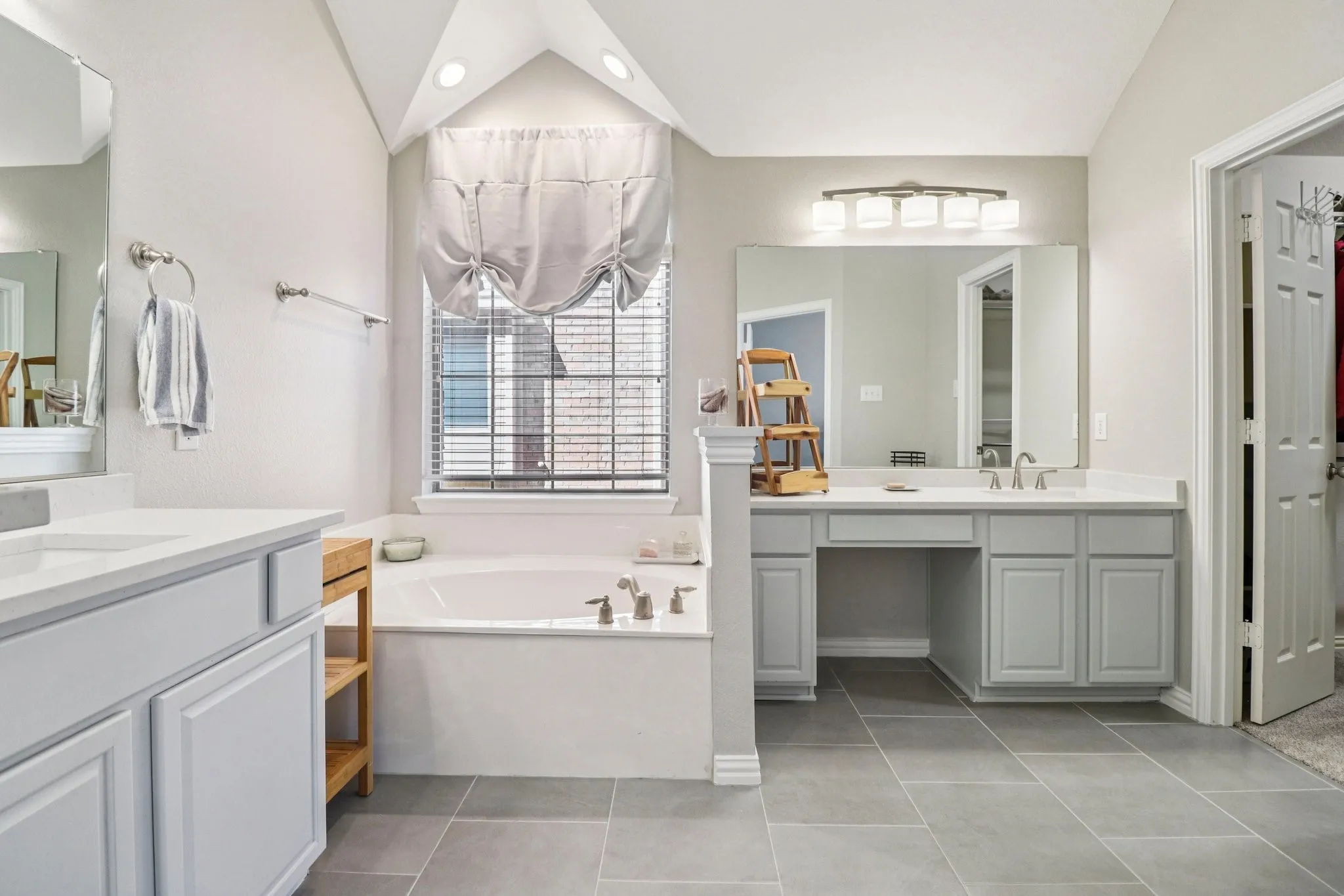 Bathroom with two vanities, a garden tub, vaulted ceiling, recessed lighting, and light tile patterned floors