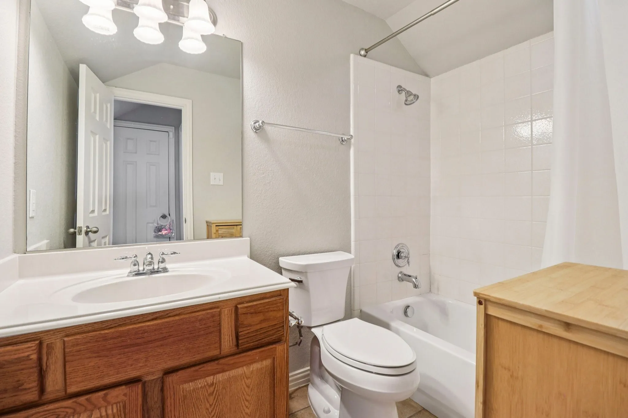 Upstairs Bathroom with vanity, a textured wall, shower / bathtub combination with curtain, and lofted ceiling