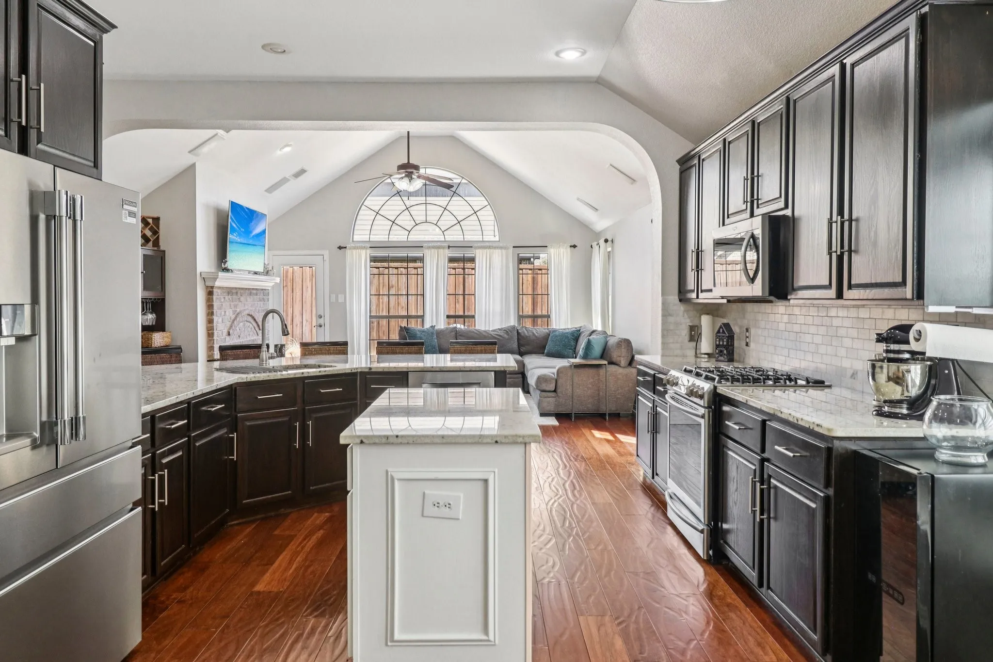 Dual tone kitchen featuring open floor plan, stainless steel appliances, light stone counters, dark wood-style flooring, and ceiling fan