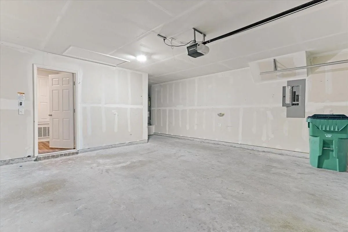 Spacious garage featuring a concrete floor, interior access door, wall-mounted electrical panel, overhead lighting, and an automatic garage door opener