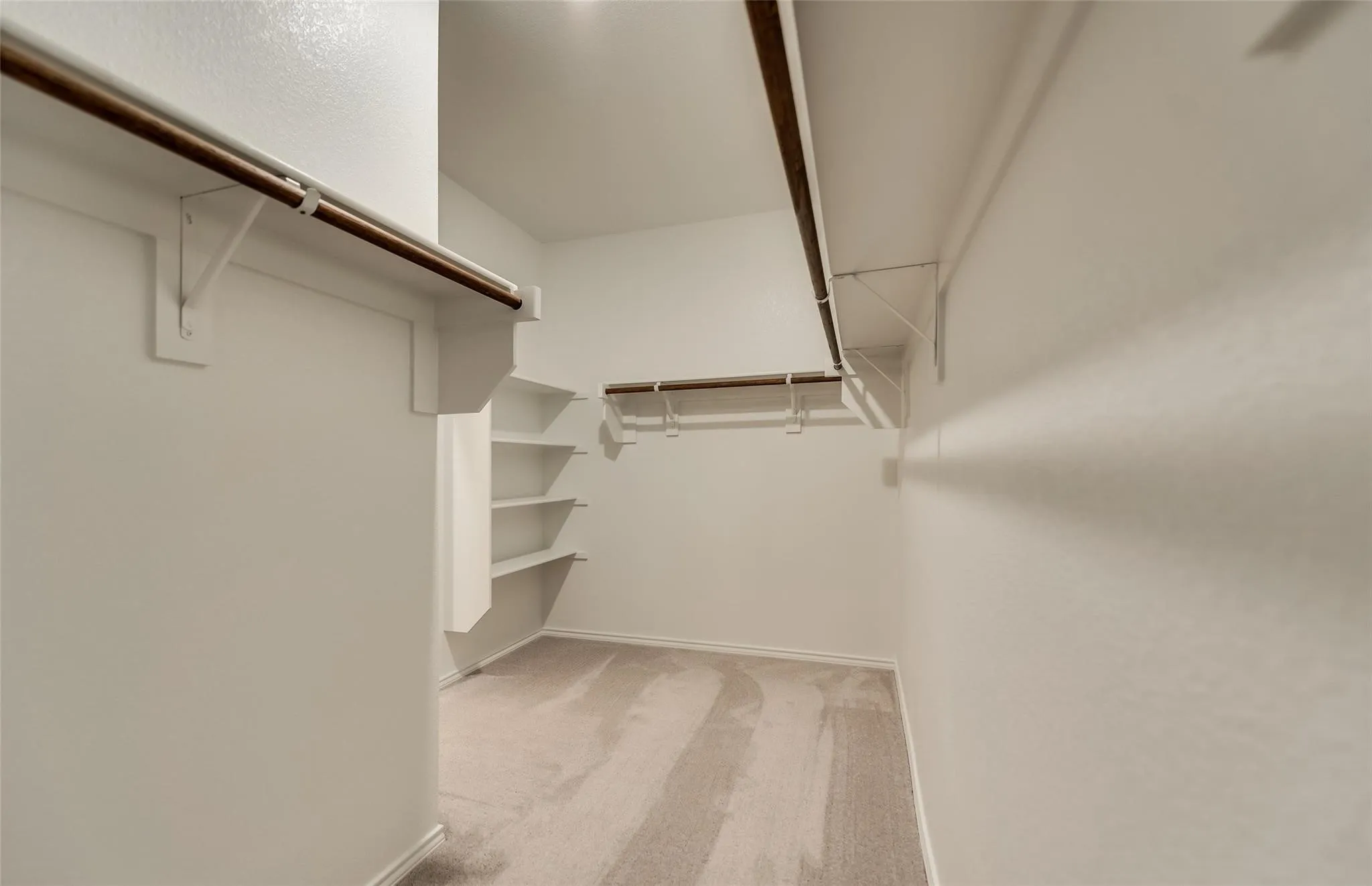 Spacious closet with light-colored carpeting, multiple hanging rods, and built-in shelving for organized storage