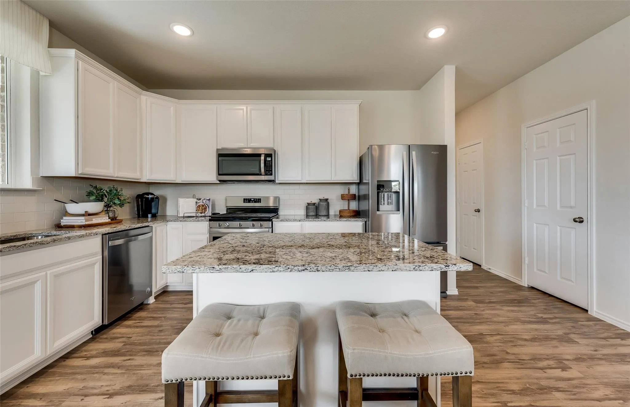 Open-concept kitchen featuring an island with stone countertop, white cabinetry, stainless steel appliances, and wood-finish flooring