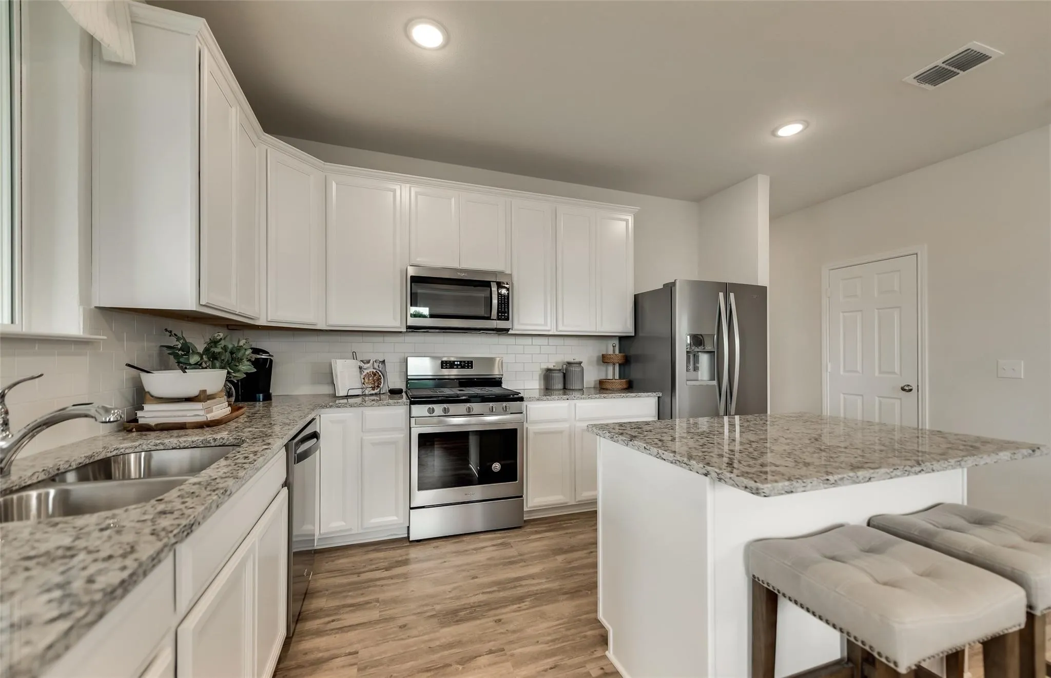 Kitchen featuring white cabinetry, stainless steel appliances, speckled stone countertops, a tile backsplash, and wood-finish flooring