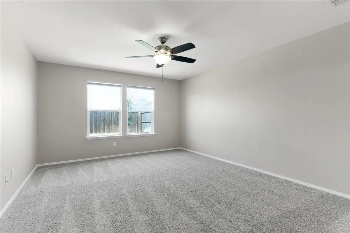 Spacious room featuring neutral paint, gray carpeting, a ceiling fan with integrated lighting, and two windows with white trim