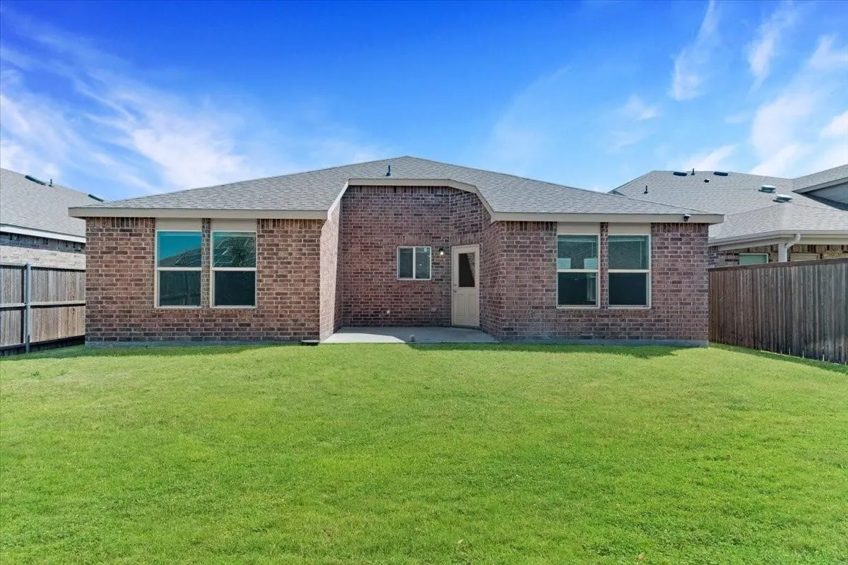 Expansive grassy backyard featuring a brick exterior, privacy fencing, a concrete patio, and multiple windows