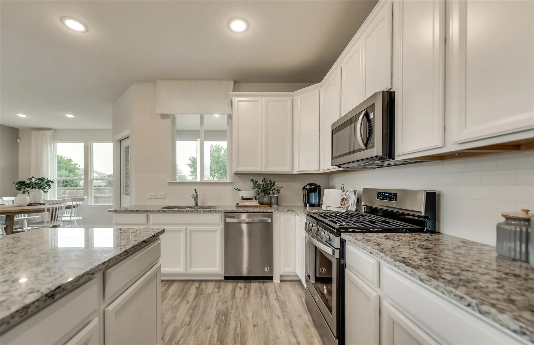Kitchen featuring white cabinetry, wood-finish flooring, stainless steel appliances, recessed lighting, and speckled countertops