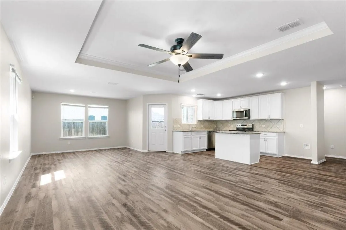 Open-concept living space featuring wood-finish flooring, a tray ceiling with a ceiling fan, recessed lighting, and multiple​​‌​​​​‌​​‌‌​‌‌​​​‌‌​‌​‌​‌​​​‌​​ windows