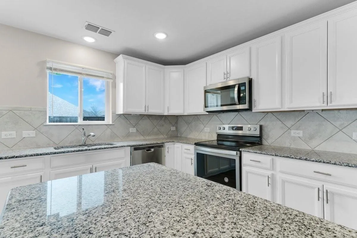 Kitchen featuring white cabinetry, granite countertops, tile backsplash, stainless steel appliances, and an undermount sink