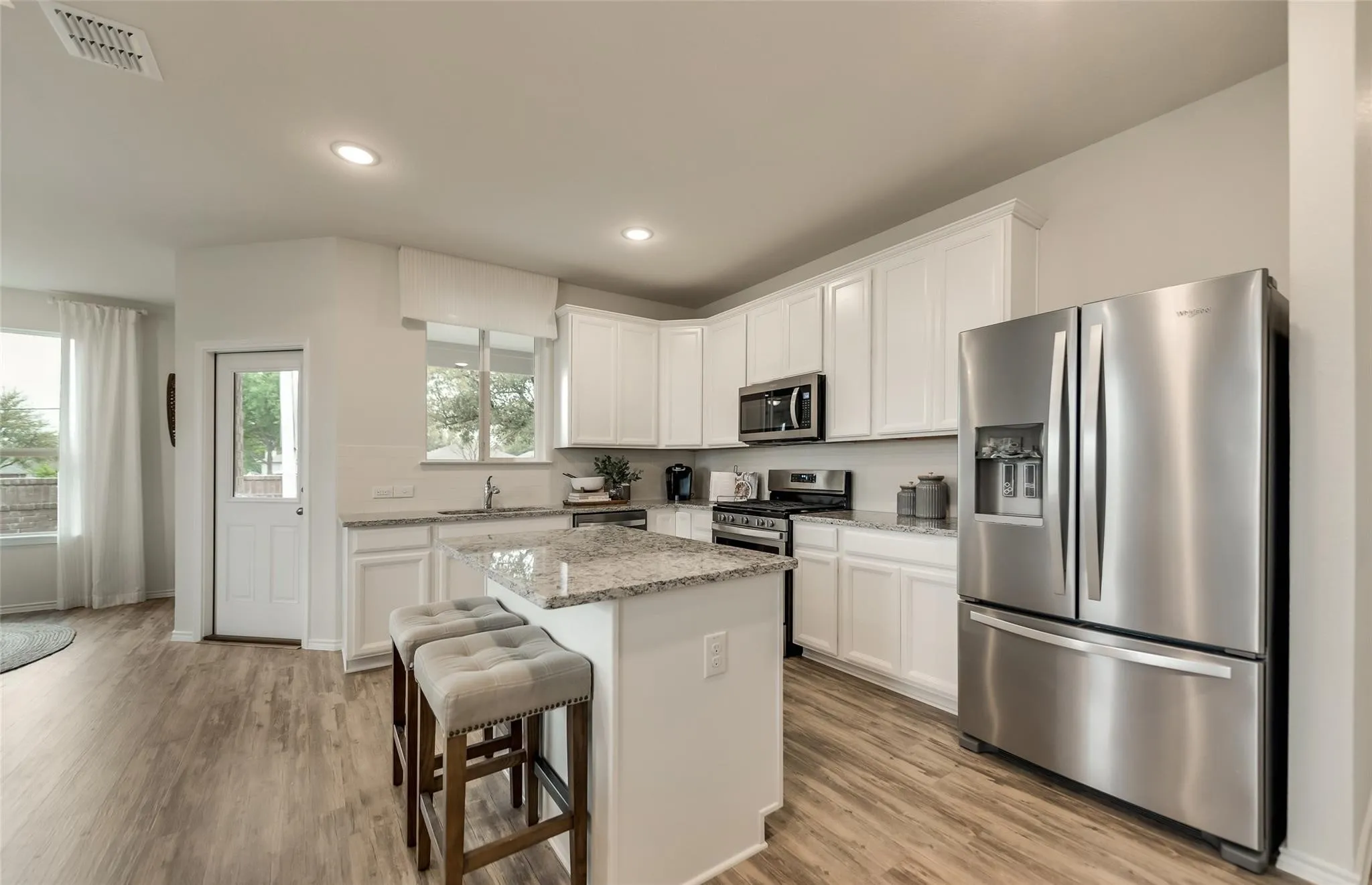 Open-concept kitchen featuring white cabinetry, granite countertops, wood-finish flooring, a stainless steel appliance suite, and a central island with seating