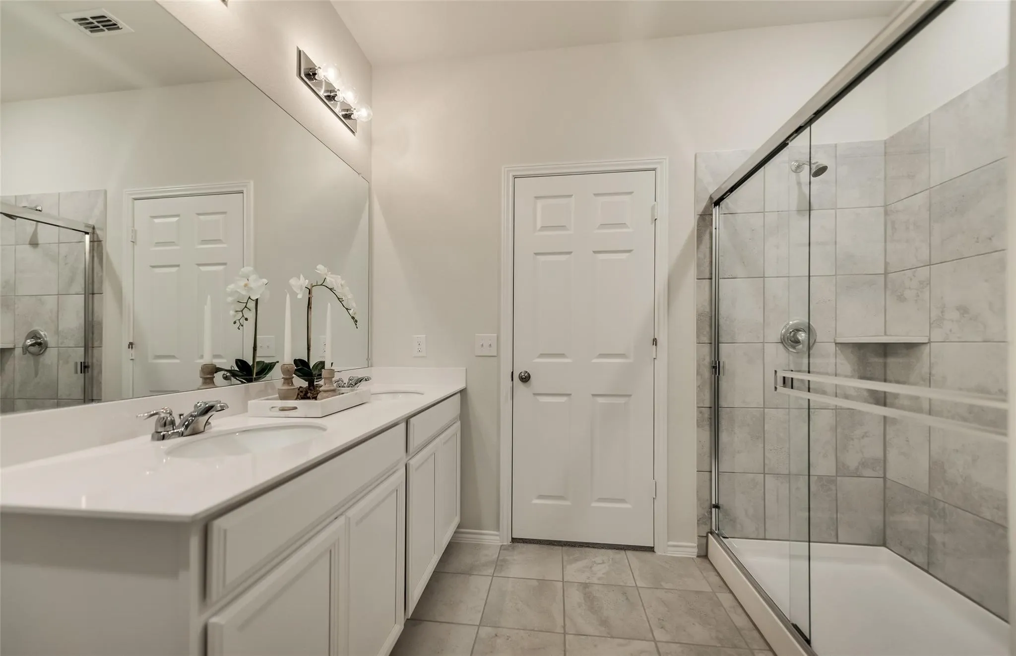 Spacious bathroom featuring a dual vanity with white cabinetry, a large vanity mirror, and a glass-enclosed shower with tiled walls and a built-in niche