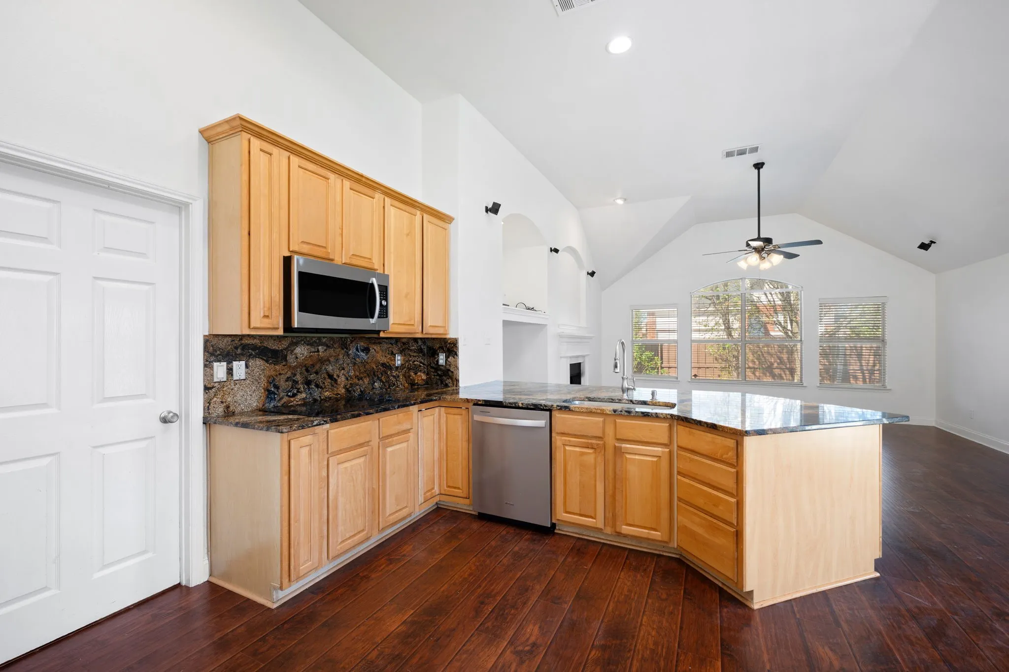 Kitchen with light wood finish cabinetry, dark stone countertops, and a peninsula