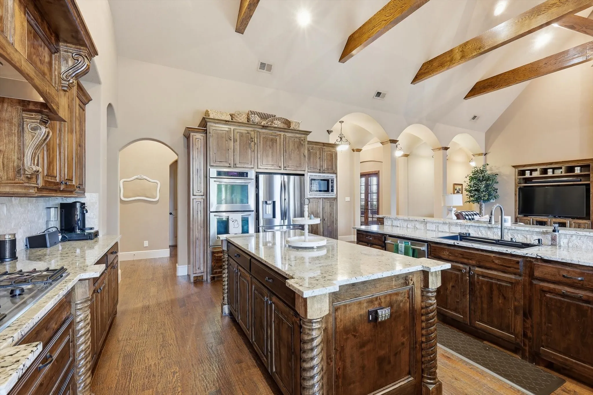 Kitchen with vaulted ceiling, light stone countertops, arched walkways, dark wood-style flooring, and stainless steel appliances
